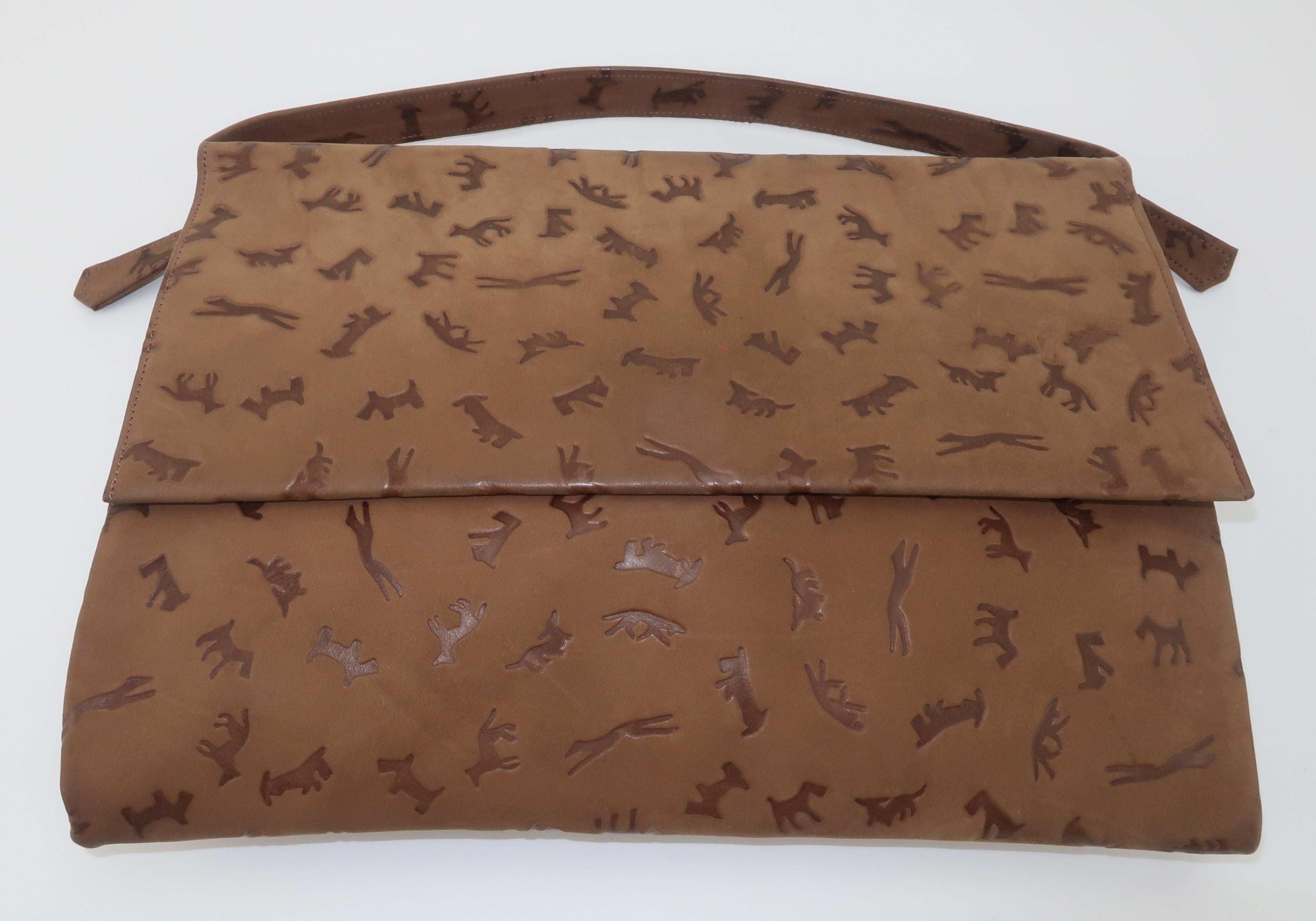 1960's Lederer brown suede envelope style handbag with an embossed pattern depicting dogs in various and witty shapes and sizes.  It has a simple top handle and snap front closure with two zippered compartments.  The interior is lined in satin with
