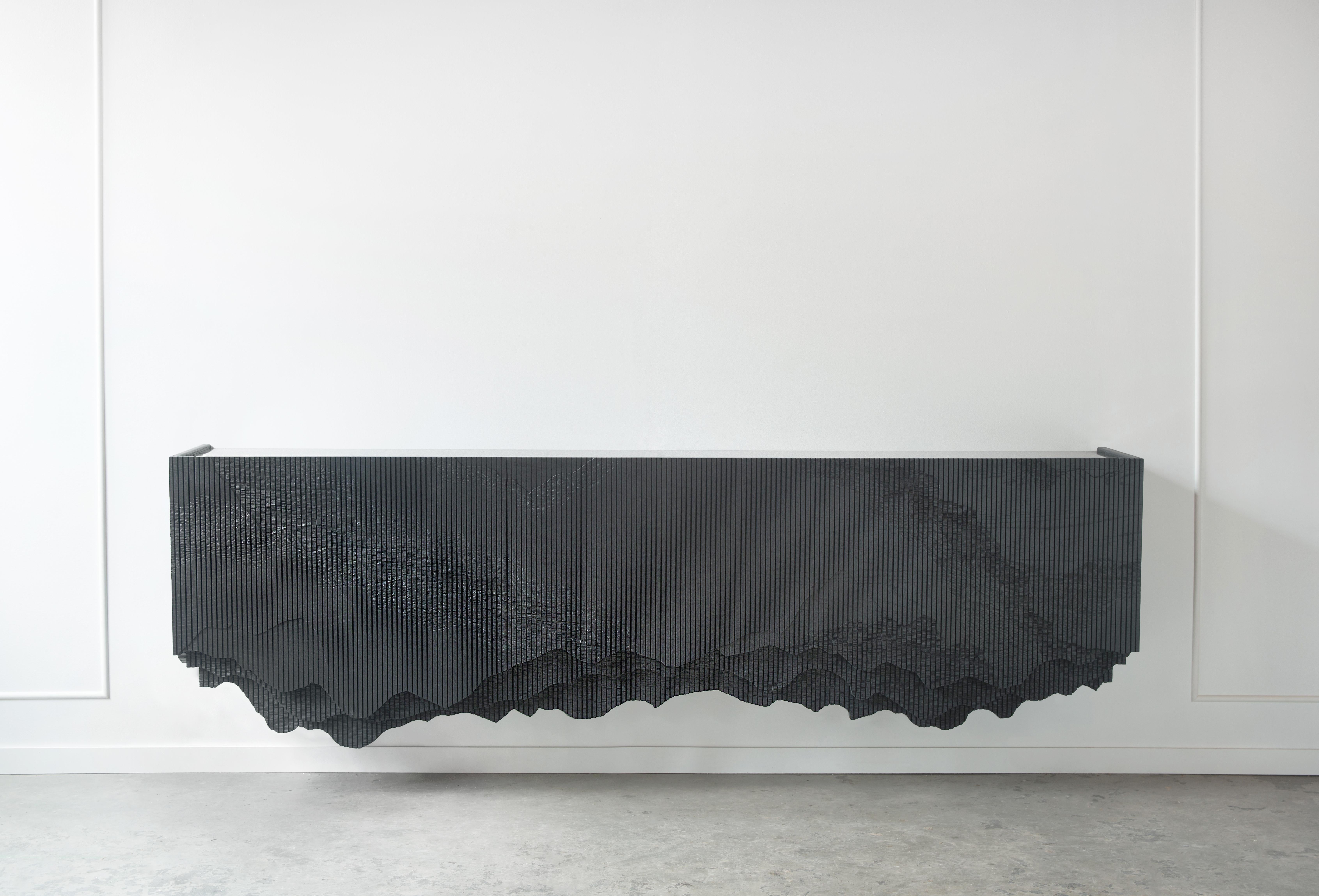 Ledge is a floating console, mounted to the wall, in solid ash with a black glass top. It stems from material exploration inspired by the cliffs around Johns’ studio, making solid ash reference crumbling stone through a unique technique. The wood
