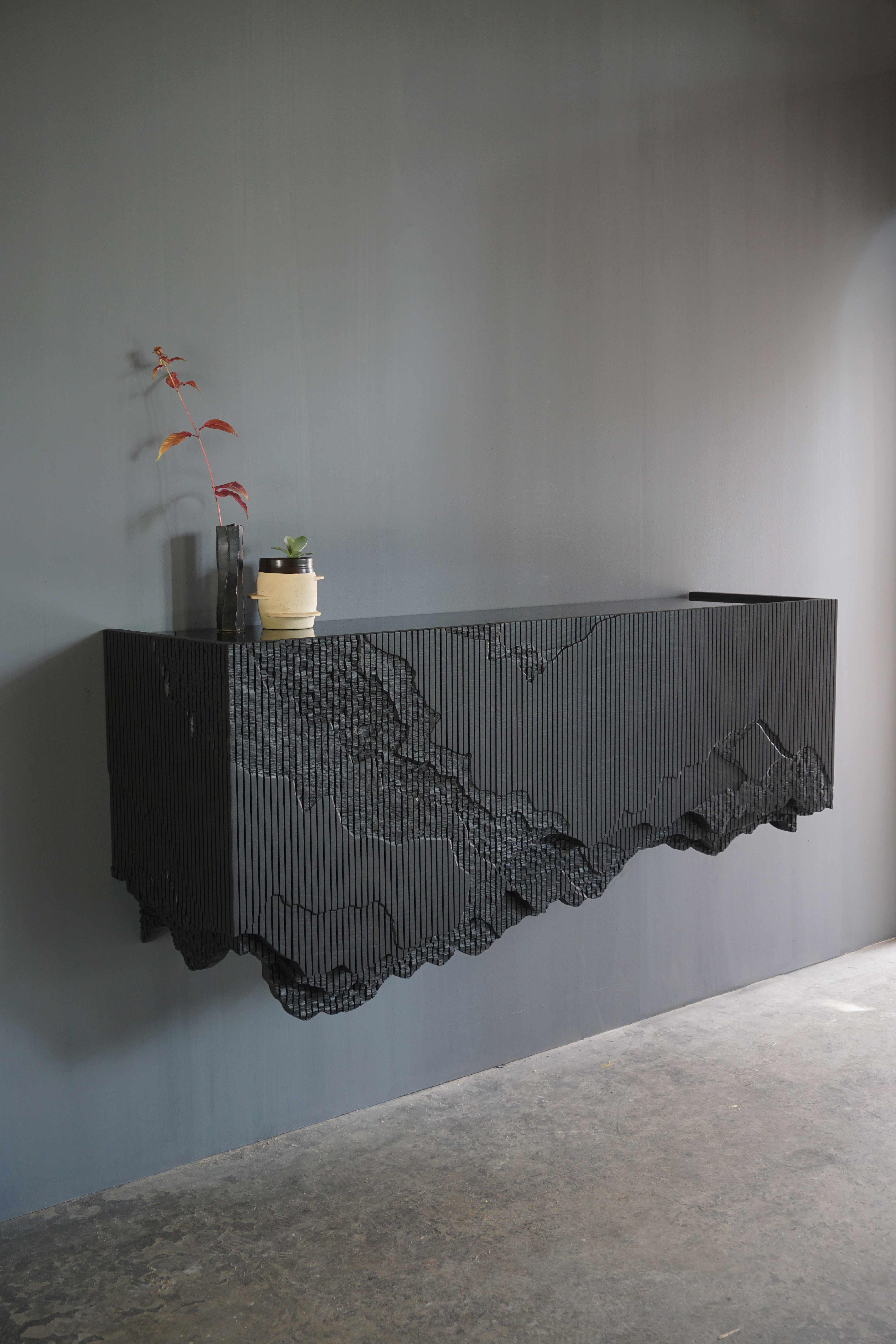 Ledge is a floating console, mounted to the wall, in solid ash with a black glass top. It stems from material exploration inspired by the cliffs around Johns’ studio, making solid ash reference crumbling stone through a unique technique. The wood