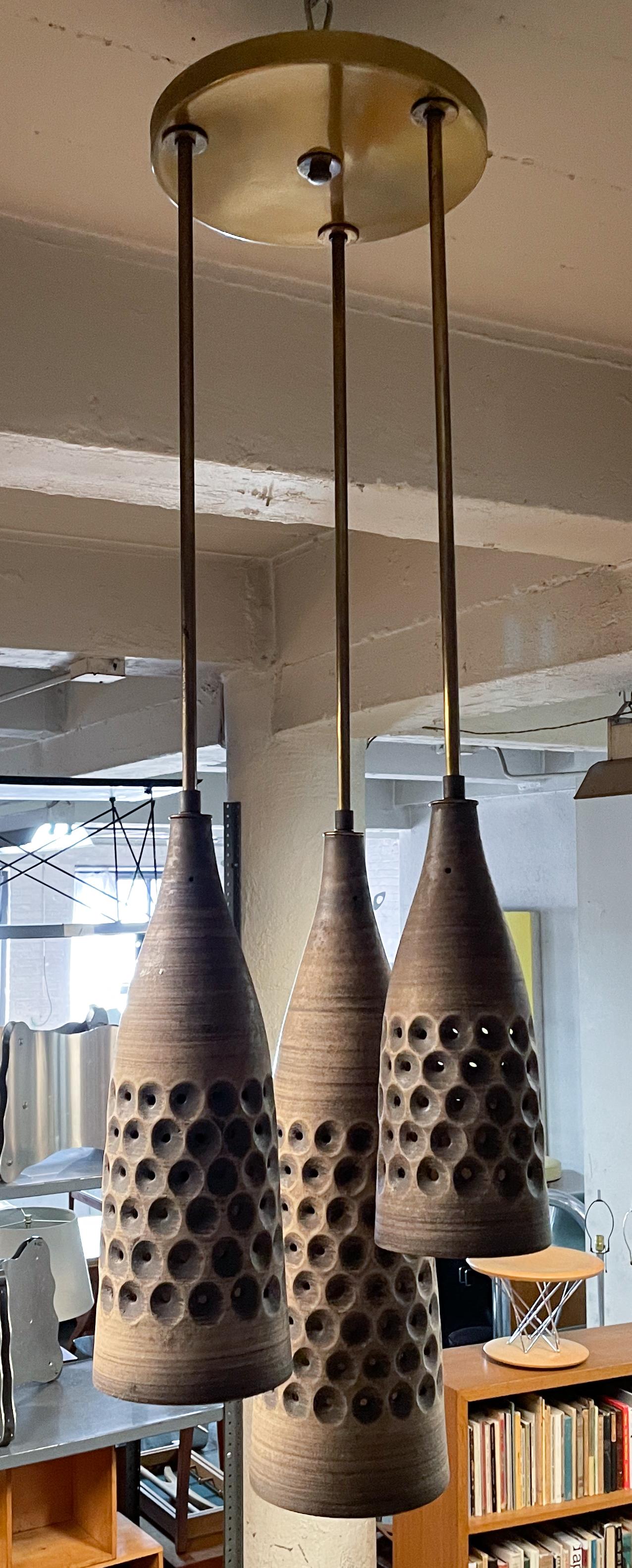 Hanging fixture in a spiral composition composed of three pierced ceramic forms of decreasing size connected by brass rods and fittings to a brass ceiling plate. Designed by Lee Rosen and made by her company Design Technics in the 1950's or early