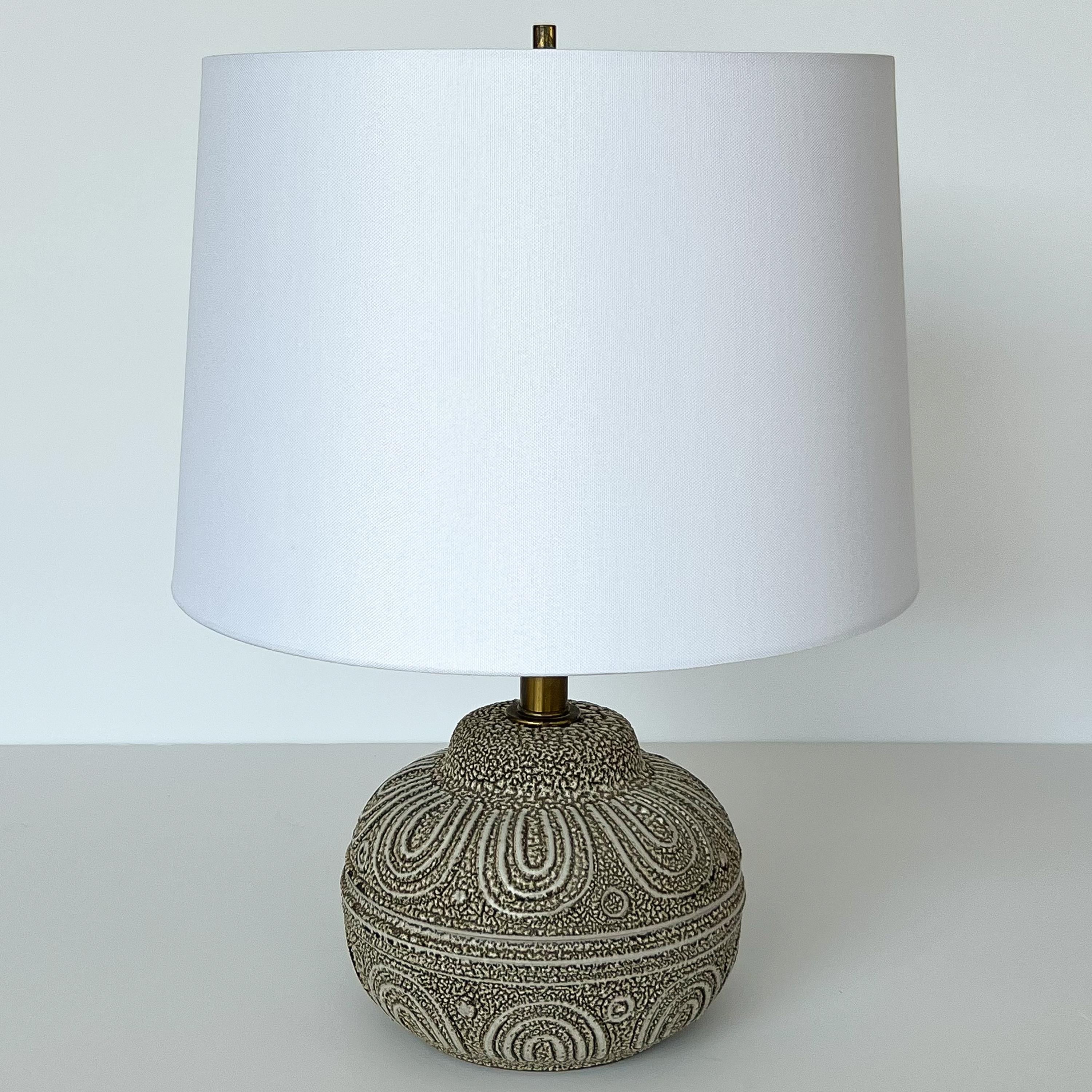 An early Lee Rosen for Design Technics textured ceramic table lamp, circa 1950s. Textured / nubby ceramic earthenware body comprised of a speckled glaze with contrasting matte lines in an abstract motif. Brass stem, harp and cylindrical finial.
