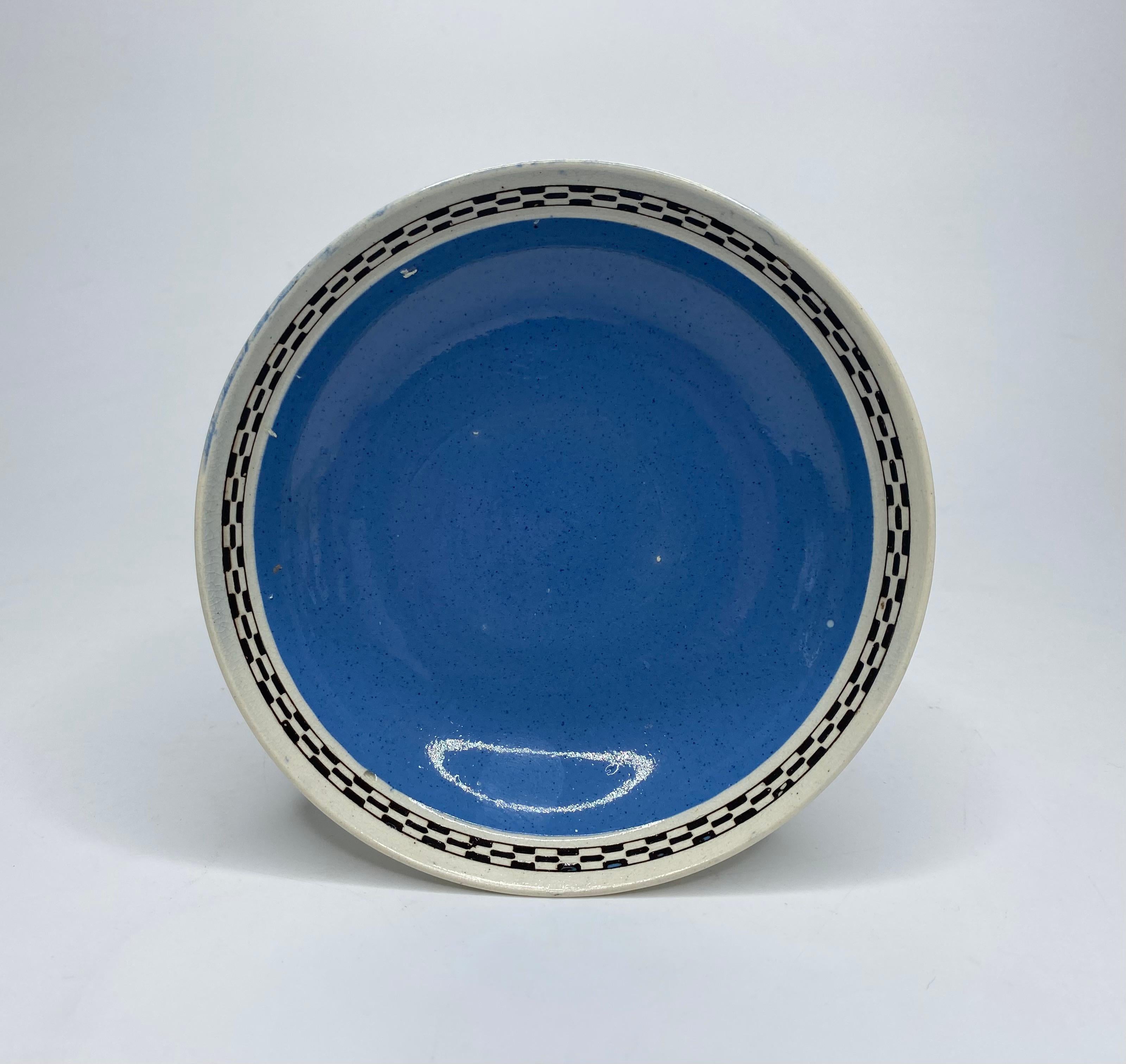 Leeds Pottery cup and saucer, c. 1790. Both pieces decorated with a broad band of powder blue slip, within a brown and white chequer board rim. All beneath a pearlware glaze.
The cup, having a fluted double strap handle, and flowerhead terminals,