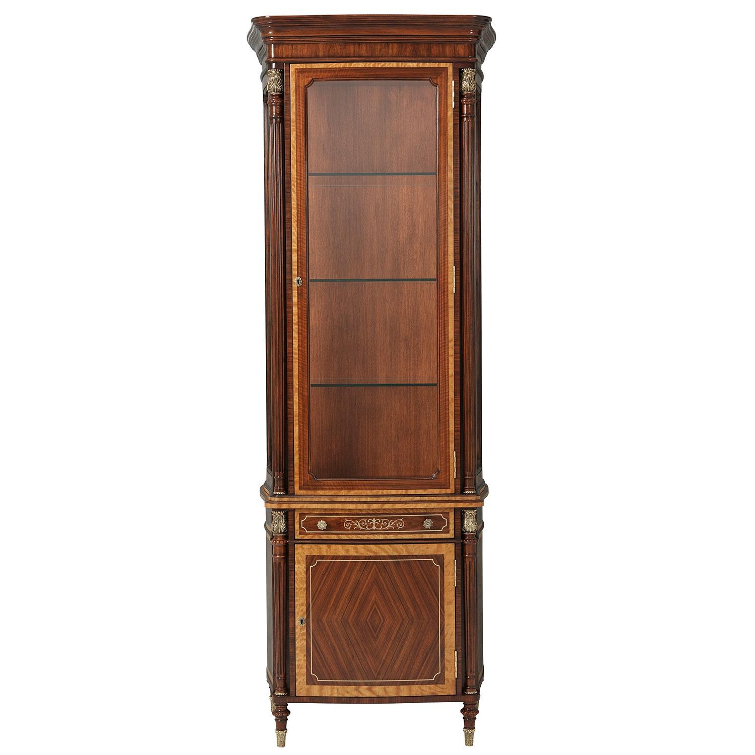 An exclusive left facing display cabinet. The meticulous construction in mahogany, adorned with floral and line brass inlay, exudes timeless elegance. The richly-figured Etimoe veneer, sourced from Central Africa, adds a touch of exotic allure to