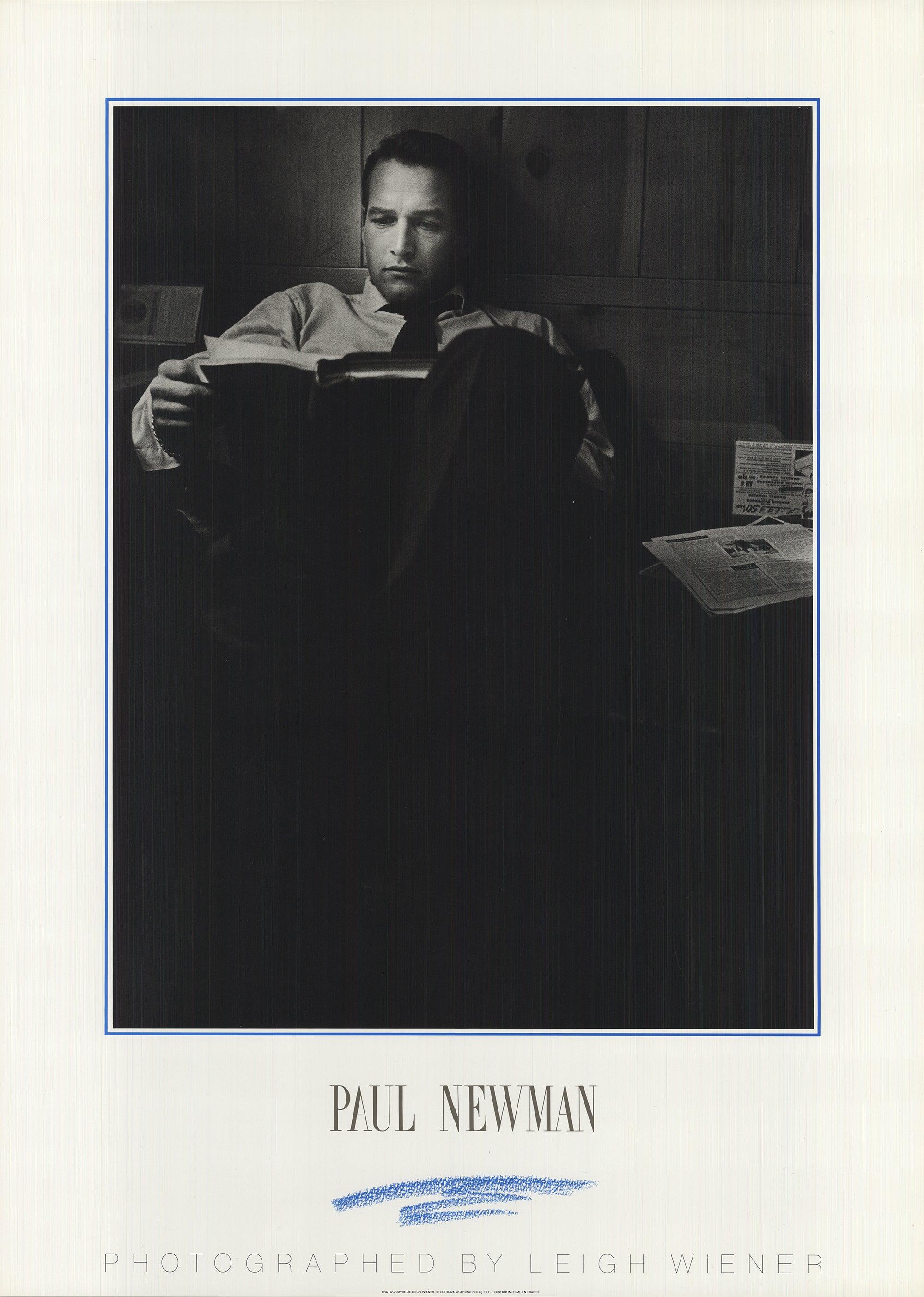 This is a reproduction of a photograph by Leigh Wiener, depicting Paul Newman seated comfortably in a chair, calmly reading a book. Published in France, the image captures a candid and introspective moment, highlighting Newman’s quiet charm and