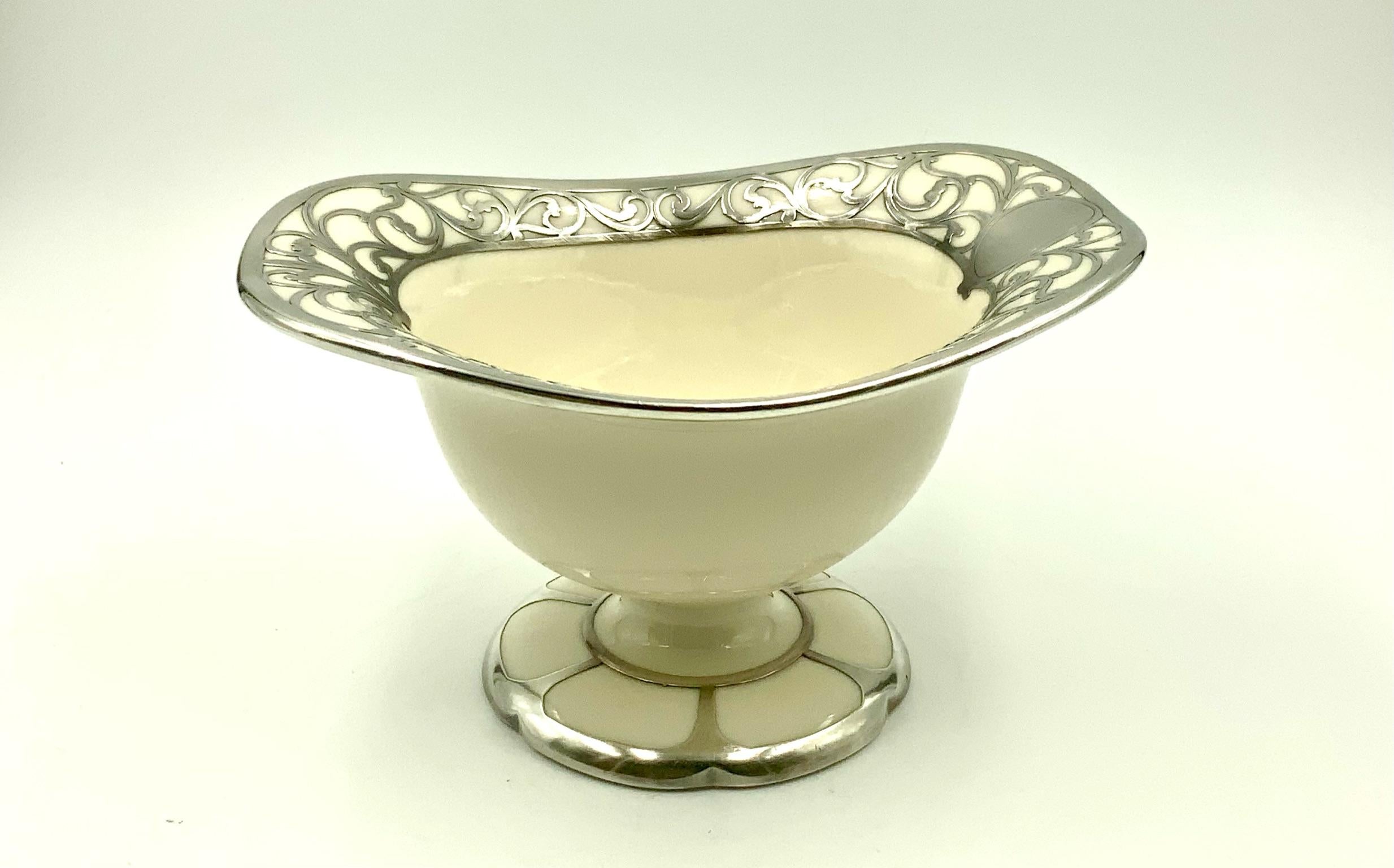 According to their site in 1910, Lenox produced their first dinnerware in belleek - the cream - colored clay body with ornate engraving. Often it is seen like this bowl with sterling silver overlay. The heavy sterling scroll design on this piece was