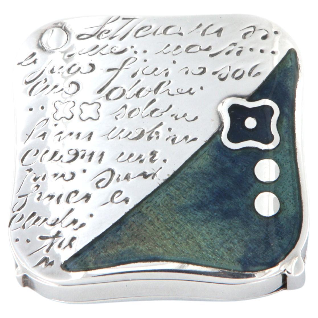 La Nouvelle Bague desk and purse lens in 925/ooo sterling silver and blue fire enamel.
Measures 4 x 4 x 1.2 cm, total weight 70 g.
Made in Italy - Florence 1997

The distinctive stylized flower-square shape first appeared in La Nouvelle Bague's