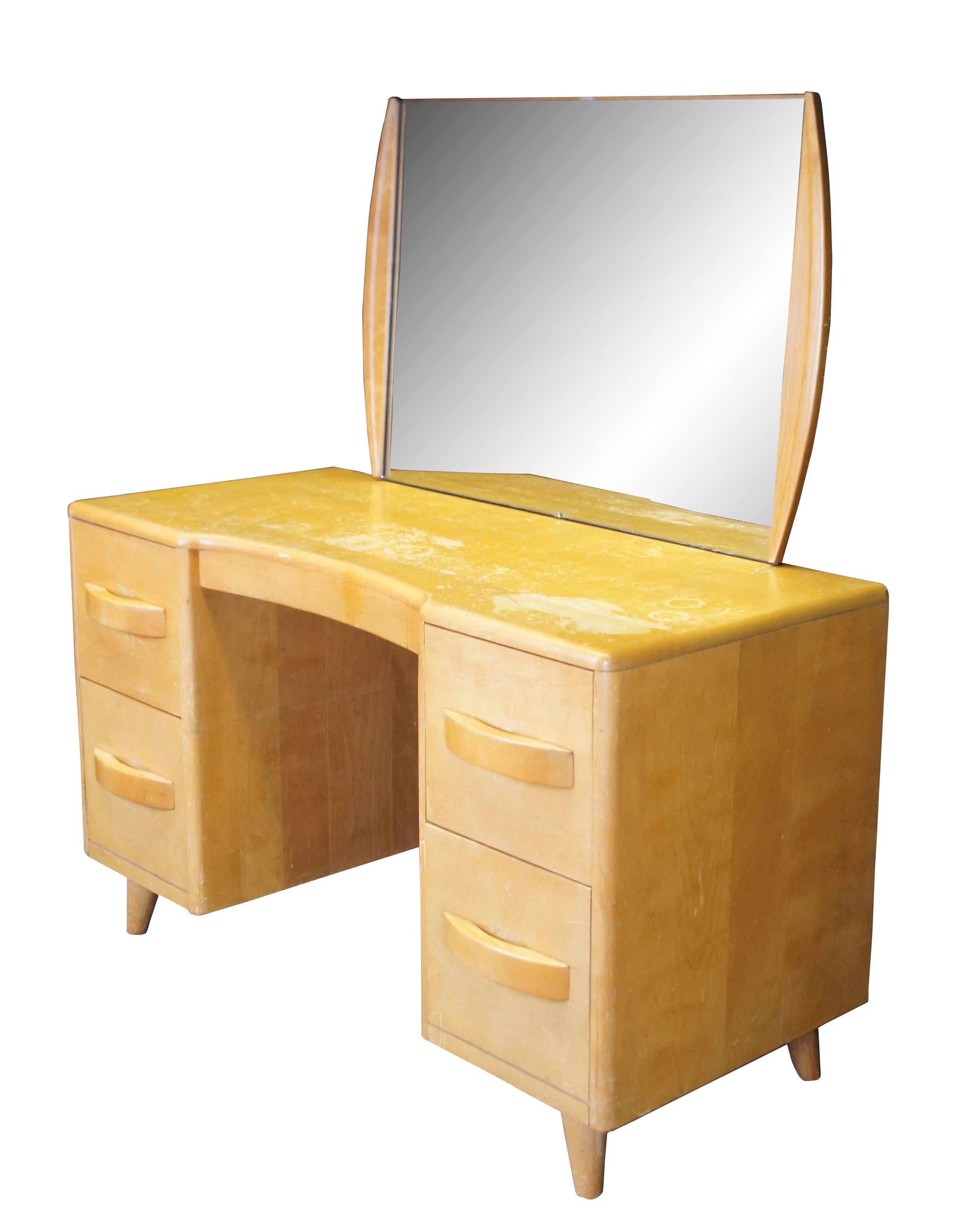 Mid century modern Leo Jiranek for Heywood Wakefield kneehole vanity desk.  Made of maple (champagne) featuring a mirrored backsplash over rectangular desk with four drawers and tapered legs.  Rockefeller Center.

LEO A. JIRANEK
Leo Jiranek (b.1900