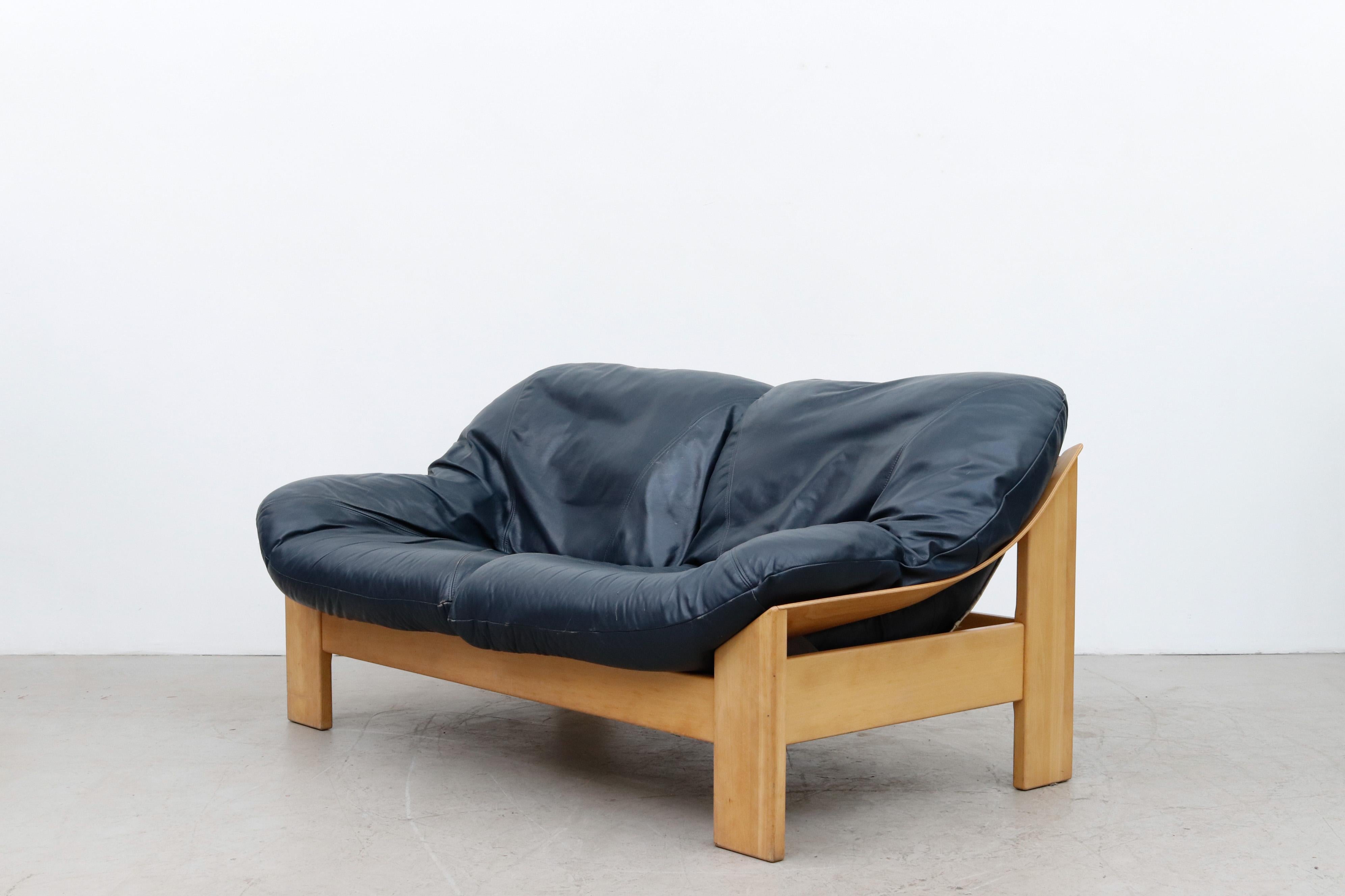 Stunning Little Leolux blue leather bucket loveseat. Two comfy blue leather cushions sit inside a natural canvas sling support. Light oak frame, all in original condition, with some wear consistent with its age and use.