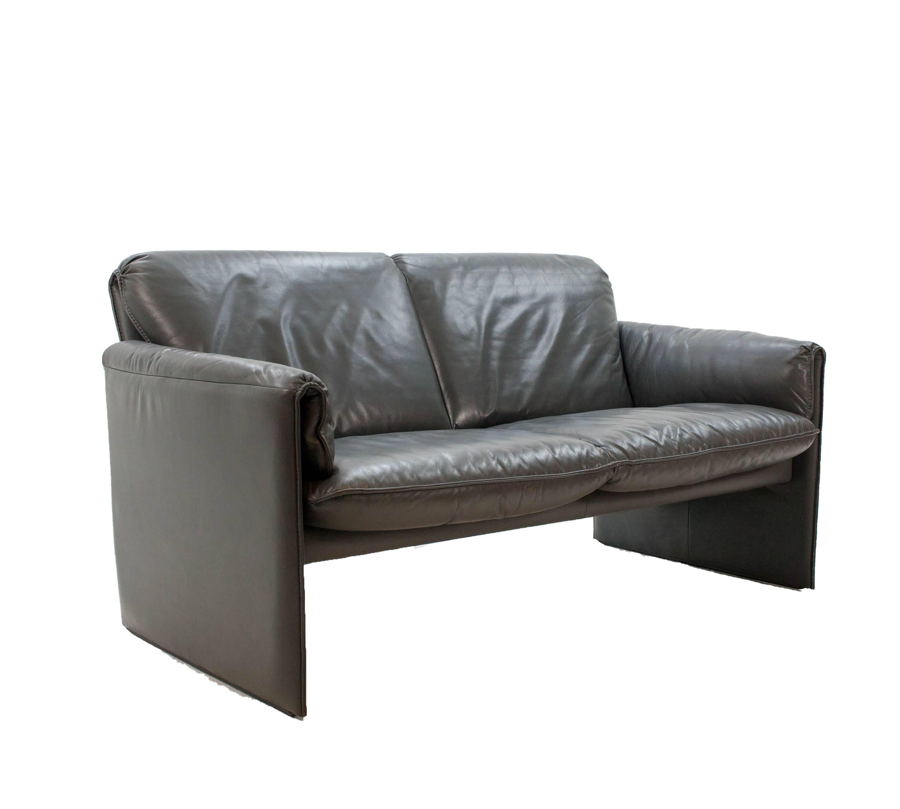 Airy and subtle loveseat in anthracite leather with white contrast stitching. These sofas have been in production for 35 years straight and are still favorites due to their great comfort and good understated design.