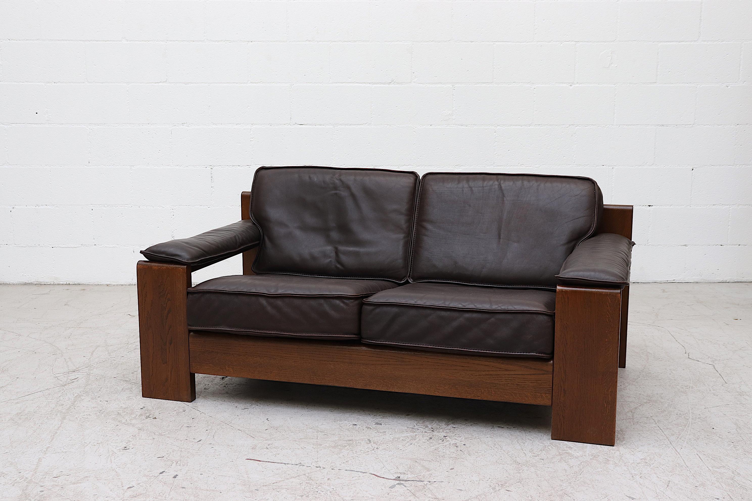 Handsome dark oak framed Leolux loveseat with beautifully worn espresso leather cushions. Armrests snap on, a snap may be missing on one armrest. In original condition with wear consistent with its age and use. Shot with matching 3-seat sofa
