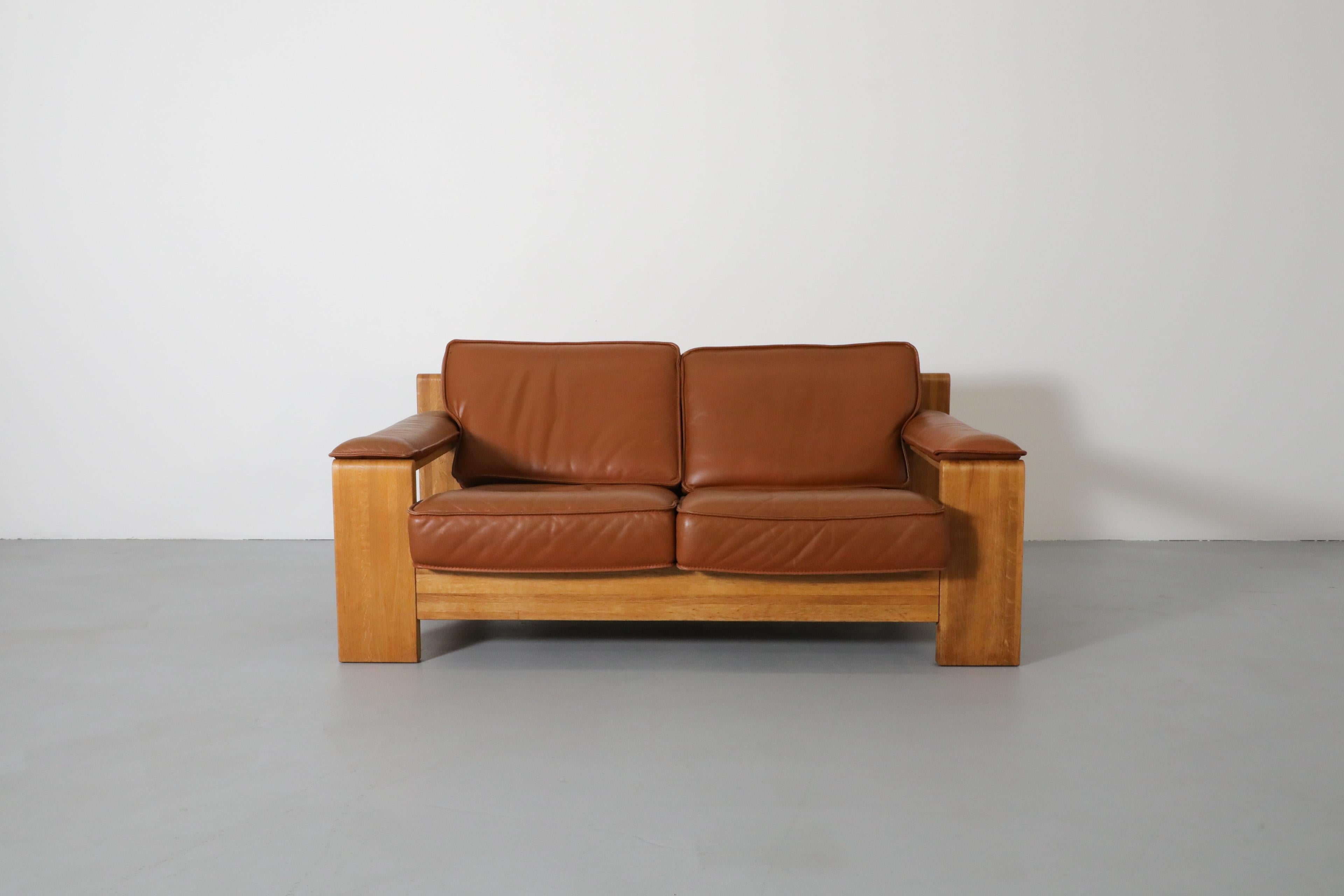 Sillón de dos plazas Classic Leolux con estructura de roble macizo y piel natural de color teja sobre soporte de lona. Bonito tono de roble claro con vetas atractivas y pátina clara. Los reposabrazos acolchados de cuero se encajan en el armazón,