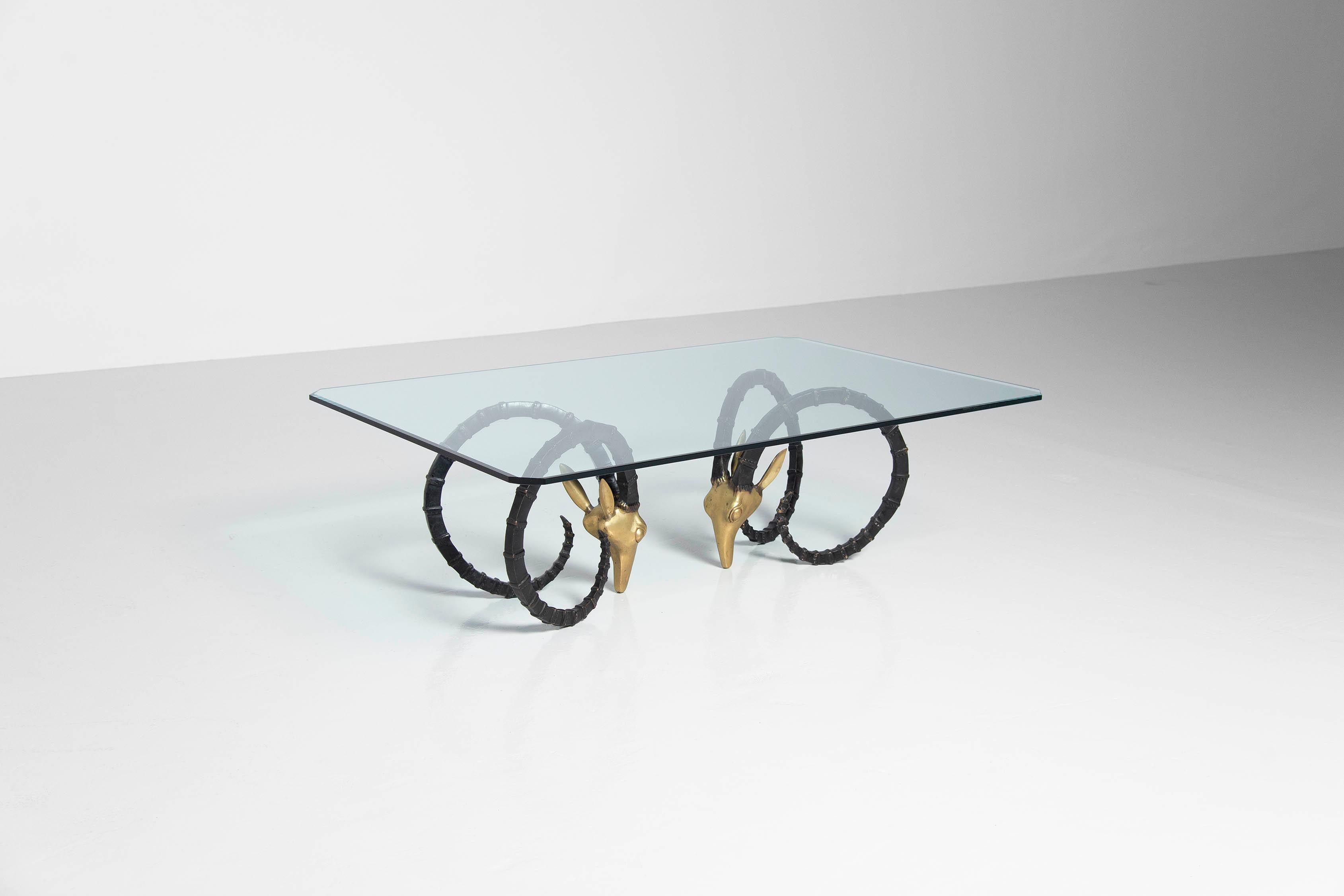 Dramatic glass top table with a pair of bronze ram head bases attributed to Leon Francois Chervet, France 1970. The glass has beveled edges and cut corners. The bronze base was made in a polished brass finish which is partly black patinated, massive