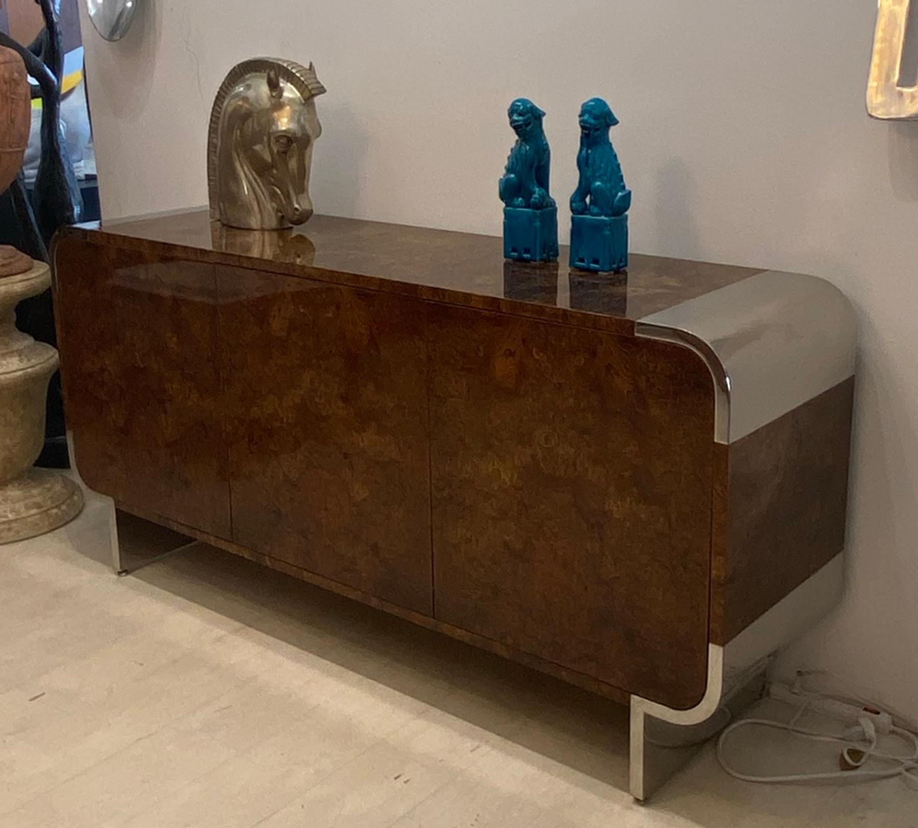 Burl credenza by Leon Rosen for the Pace Collection. Beautiful burl wood veneer polished steel rounded waterfall corners and legs. High gloss lacquer finish. Three push open doors. Three pull out drawers with three adjustable shelves below. Finished