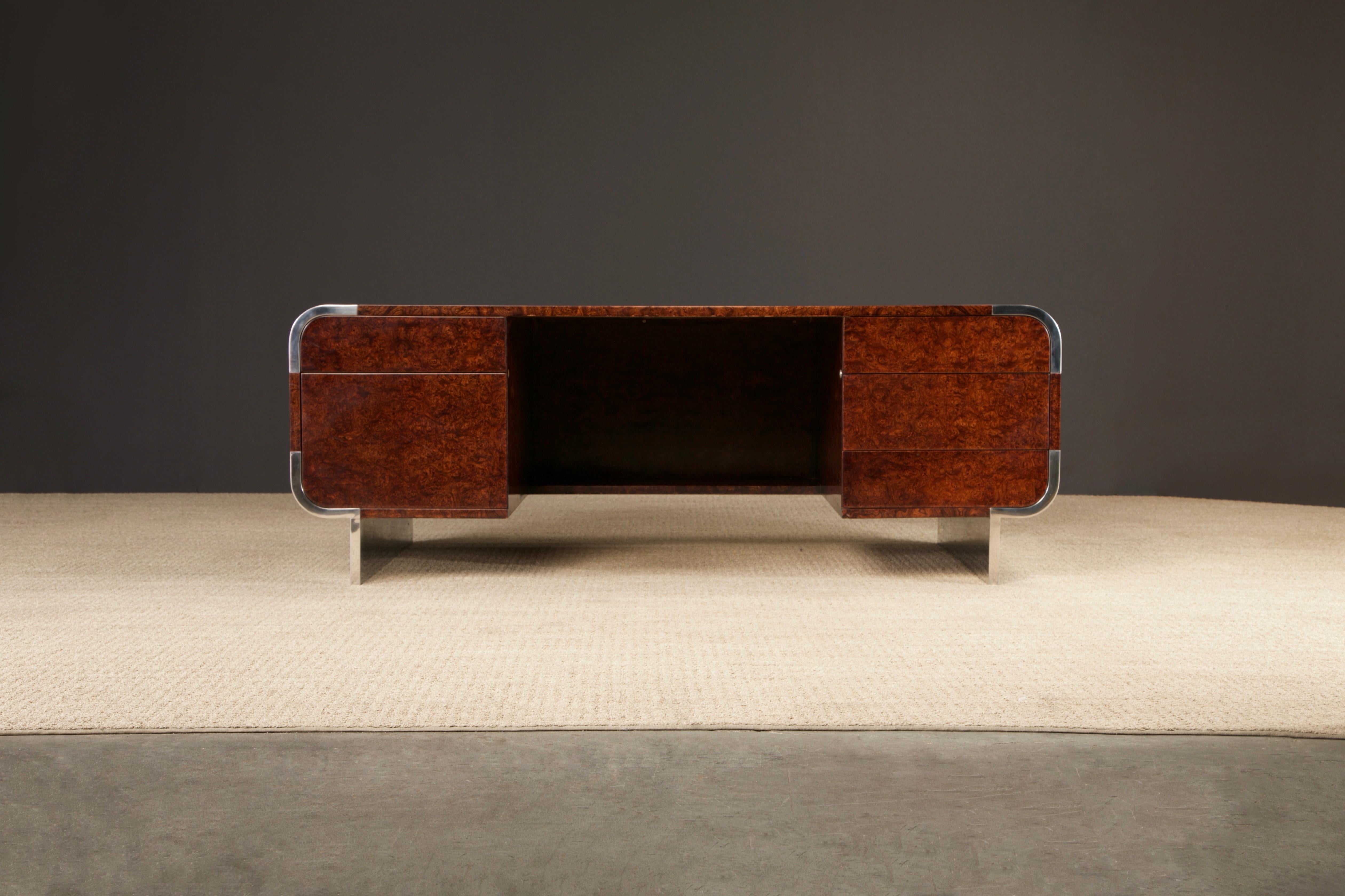 This grand executive desk by Leon Rosen for Pace features an exotic Rosewood colored burlwood floating top and drawers with polished stainless steel waterfall trim, legs and accents. Designed and made in the 1970s and 1980s by Pace Furniture known