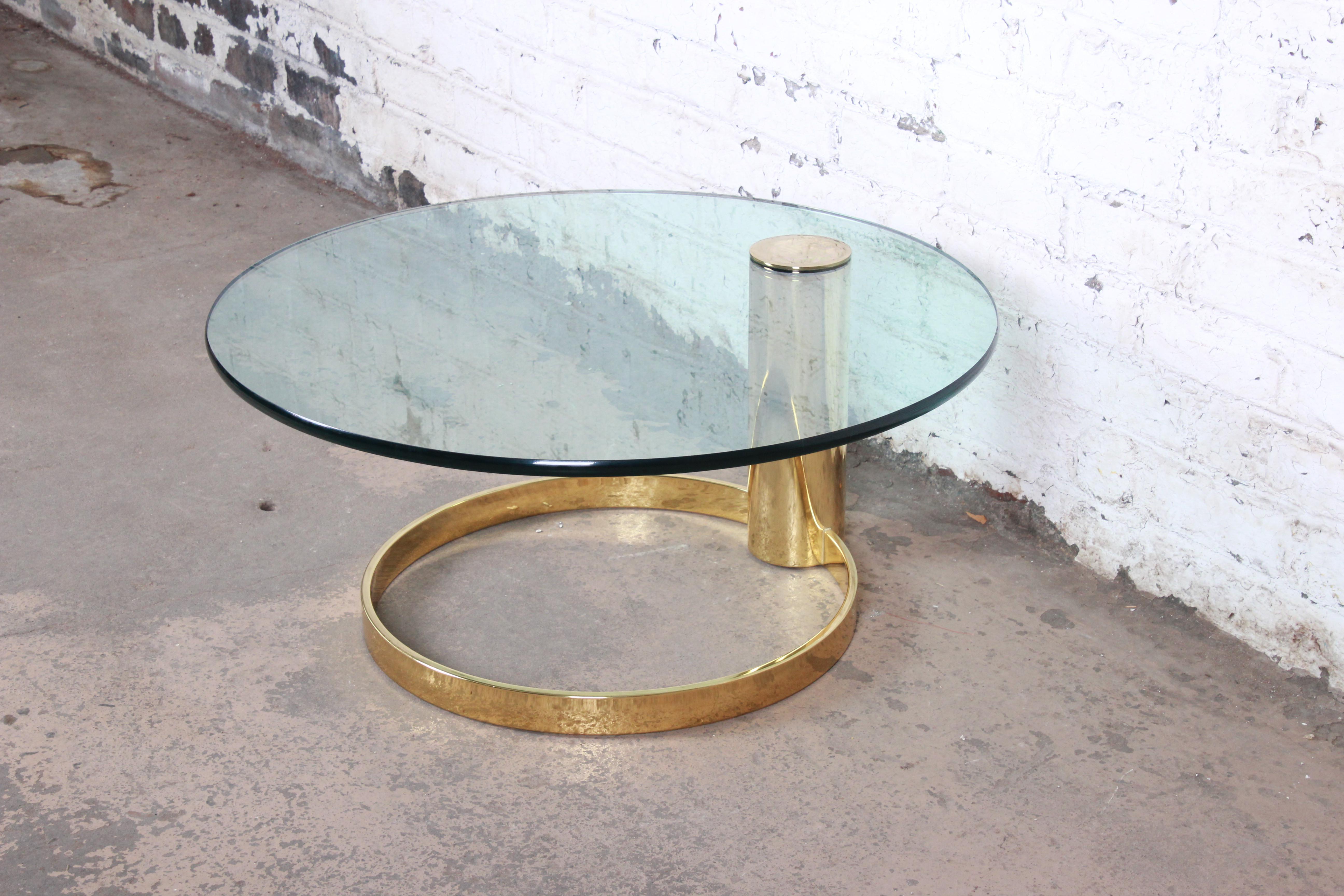 An exceptional Mid-Century Modern Hollywood Regency brass and glass coffee table designed by Leon Rosen for the Pace Collection. The table features a circular brass base with a single brass pedestal and a thick cantilevered glass top. An excellent