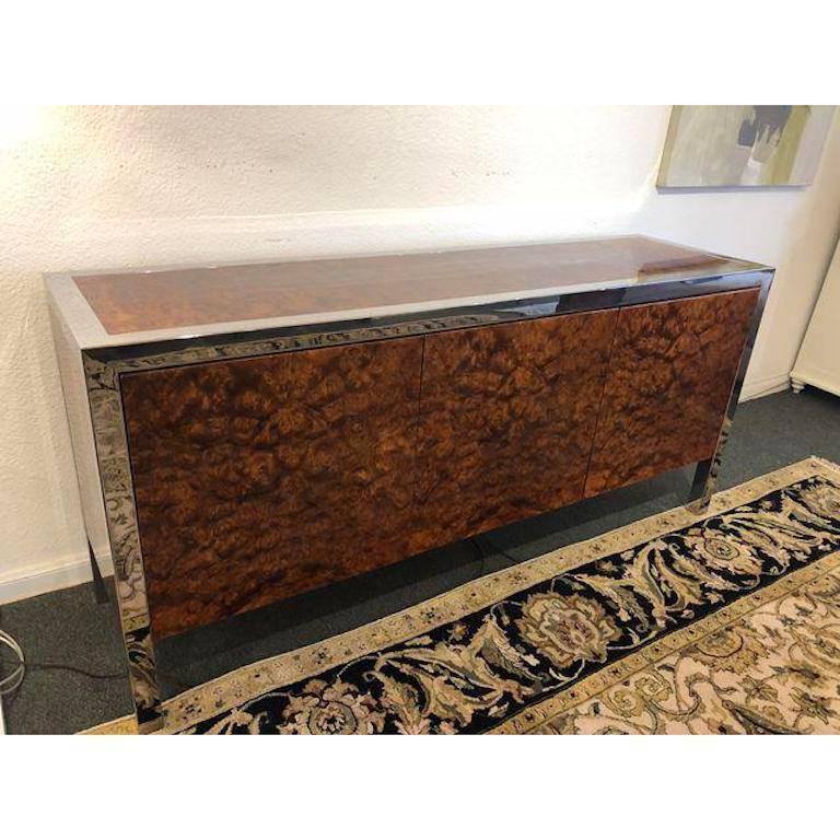 An exquisite executive credenza by Leon Rosen for Pace Collection. Crisply framed in polished stainless steel, the credenza oozes success in rich olive wood burl. Ample storage includes, drawer, file drawer and adjustable shelving behind beautiful