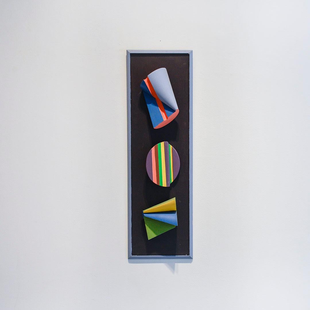 Abstract geometric three dimensional wall sculpture in black, blue, purple and green, with accents of yellow and pink
