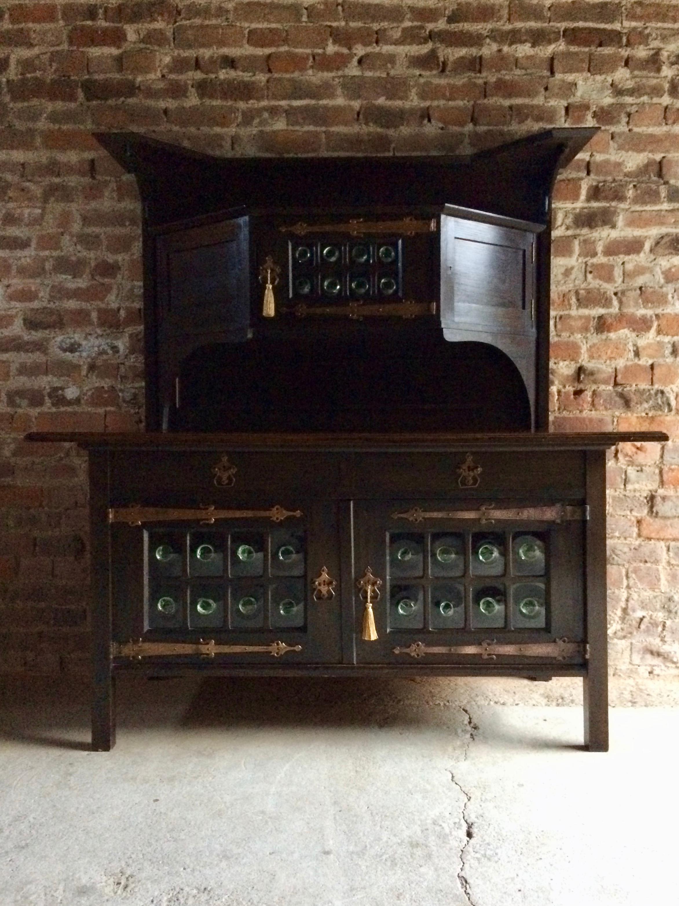 Magnificent statement piece in the Manner of Leonard Wyburd for Liberty & Co, an oak Arts & Crafts sideboard dresser circa 1920, with bottle eye glazing to doors, the super structure with two angled side cupboards and one central bottle eyed glass