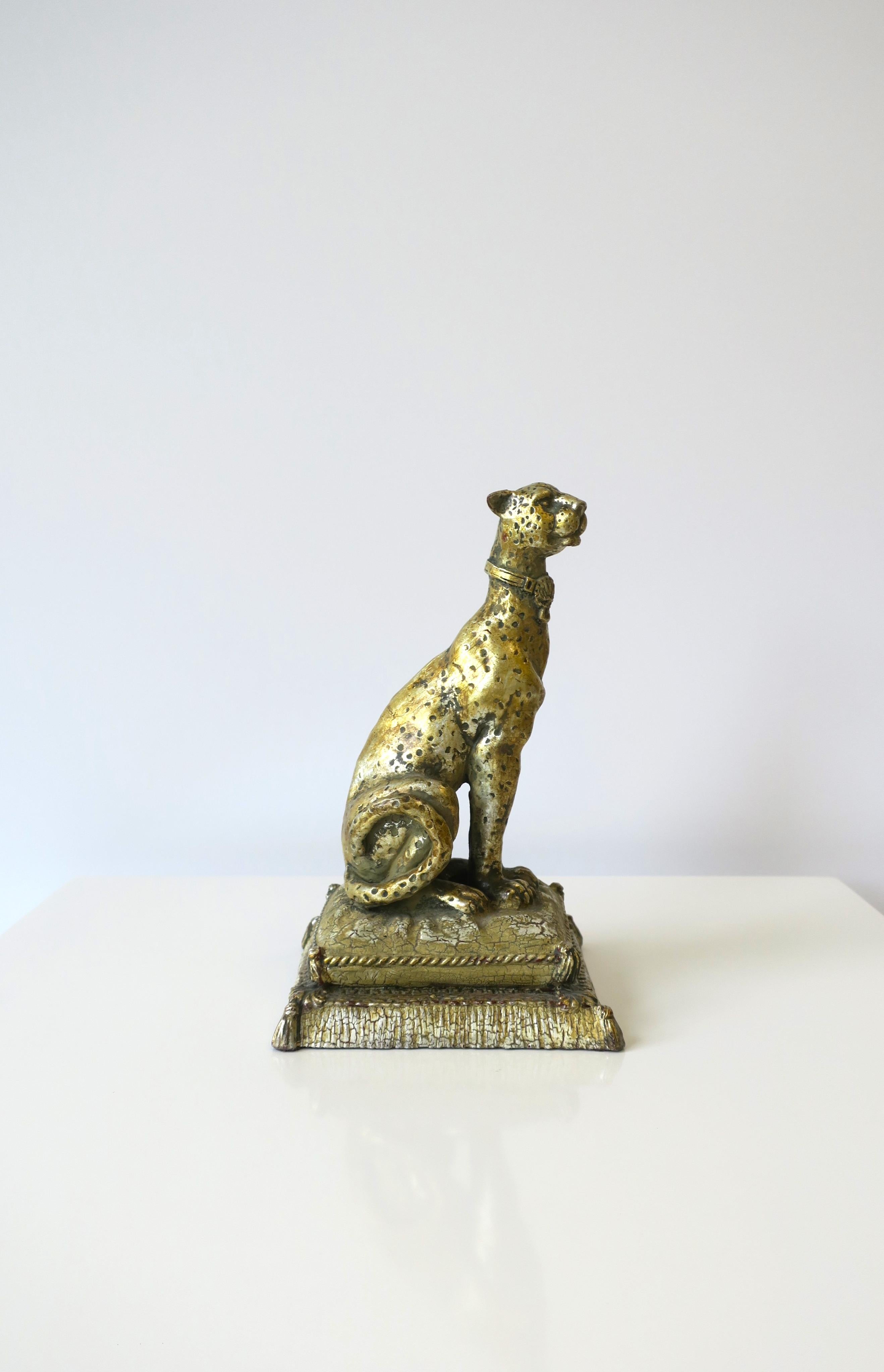 A regal Art Deco leopard cat decorative object, circa late-20th century. Leopard cat is hand-painted in gold with touches of silver, has detailed features in tail, face, collar, paws, while sitting atop a fluffy pillow with tassels. A great