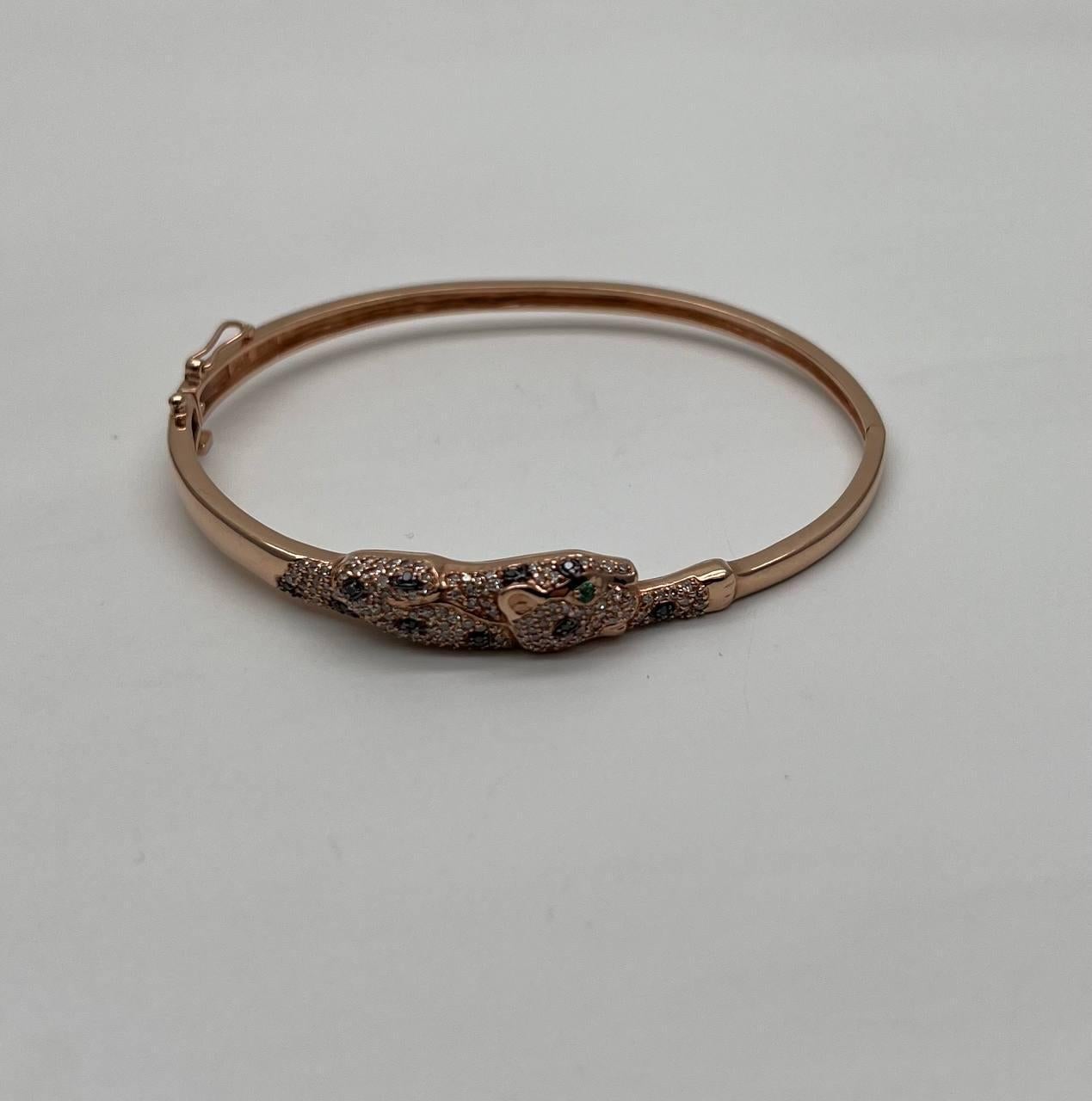 Ce bracelet exquis est doté d'une bande élégante et polie. La pièce maîtresse est un motif de panthère finement détaillé, incrusté de diamants étincelants. Les yeux de la panthère sont sertis d'émeraudes d'un vert éclatant, ajoutant un contraste