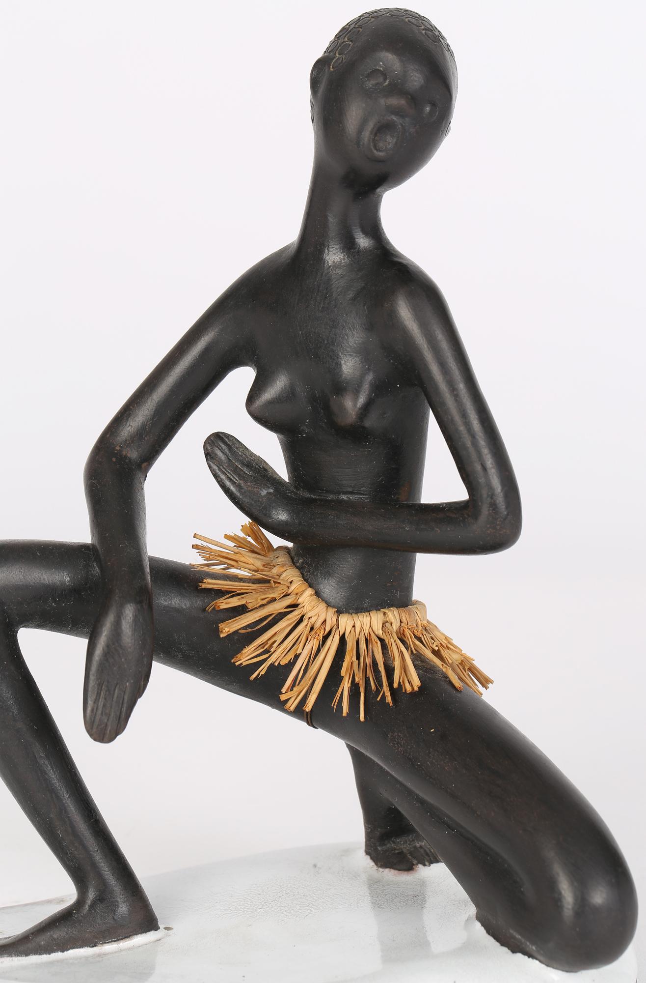 A delightful Austrian mid-century ceramic figurine portraying a nude African woman wearing a grass skirt made in Vienna by Leopold Anzengruber (1912-1979) and dating from around 1950. The woman kneels, possibly in a dance pose, on a shaped base