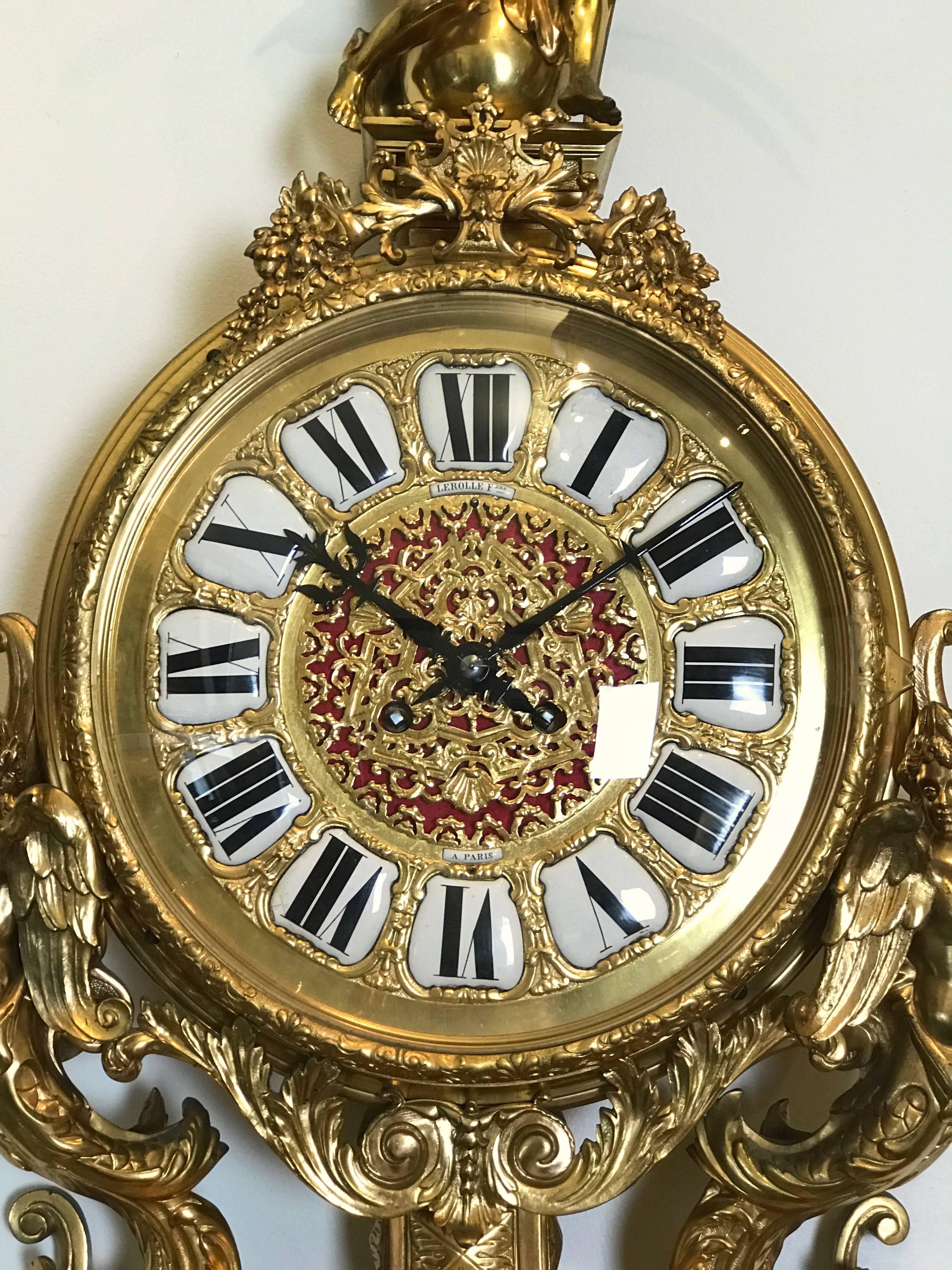 Lerolle Freres gilt bronze wall clock third quarter of the 19th century. Louis XVI style having a round face with enamel Roman numerals, supported by a pair of winged cherubs on a demilune table, over a mask of Bacchus and grapes. And having a