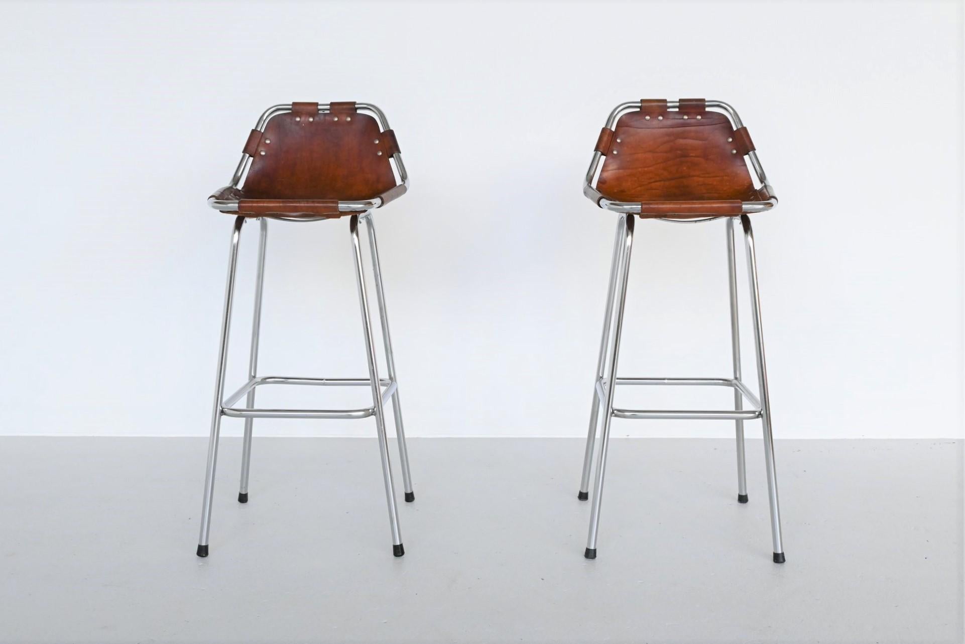 Set of 2 great shaped bar stools used by Charlotte Perriand for Les Arcs ski resort, France 1960. The stools have chrome plated tubular metal frames and thick natural leather seats with nice patina of usage. They are strong, comfortable and look