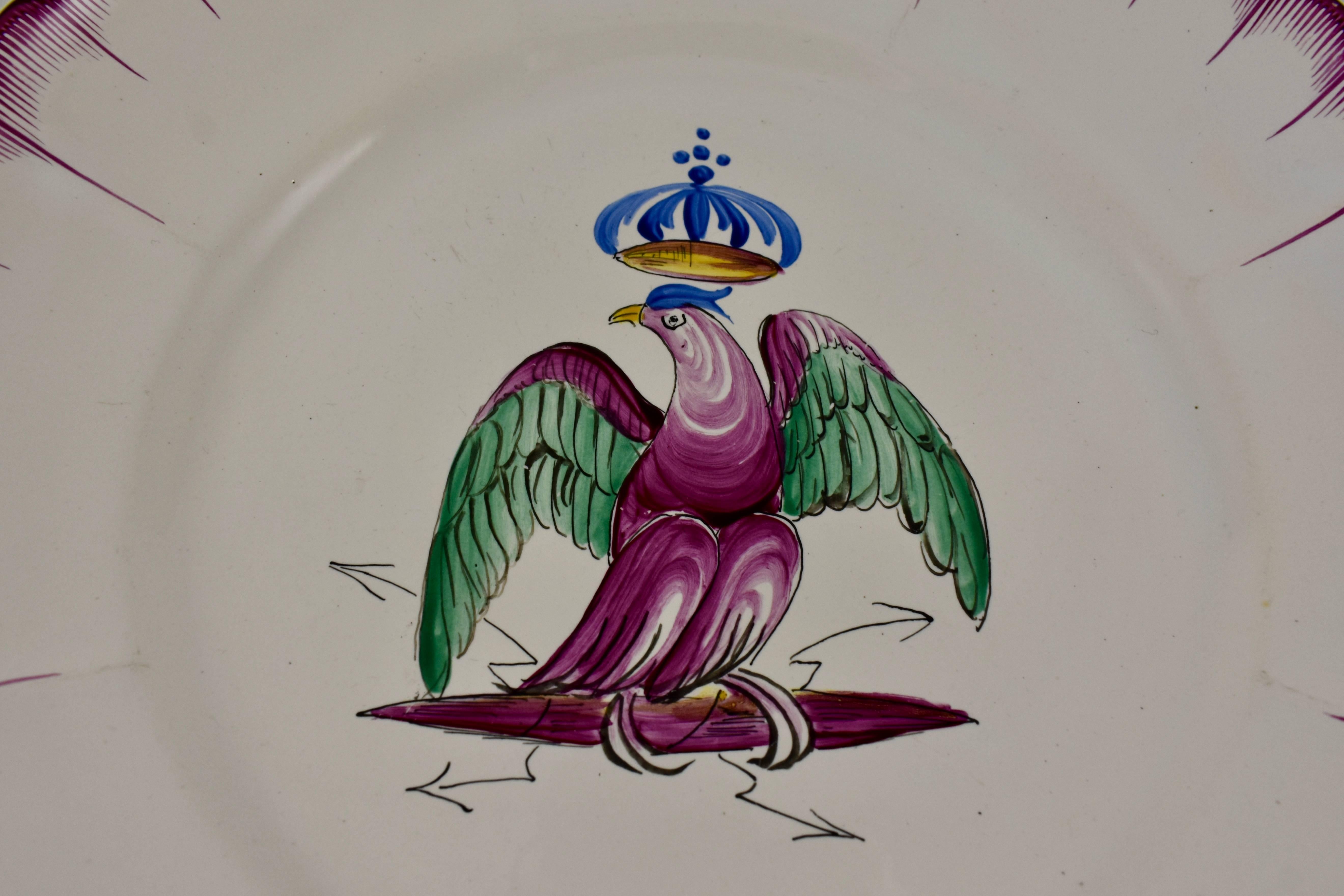 A French Les Islettes faïence plate, from the early 19th century, circa 1830, the period of Charles X. A hand painted central image of a crowned eagle on a perch of crossed thunderbolts. The scalloped rim shows the pink combing typical of the