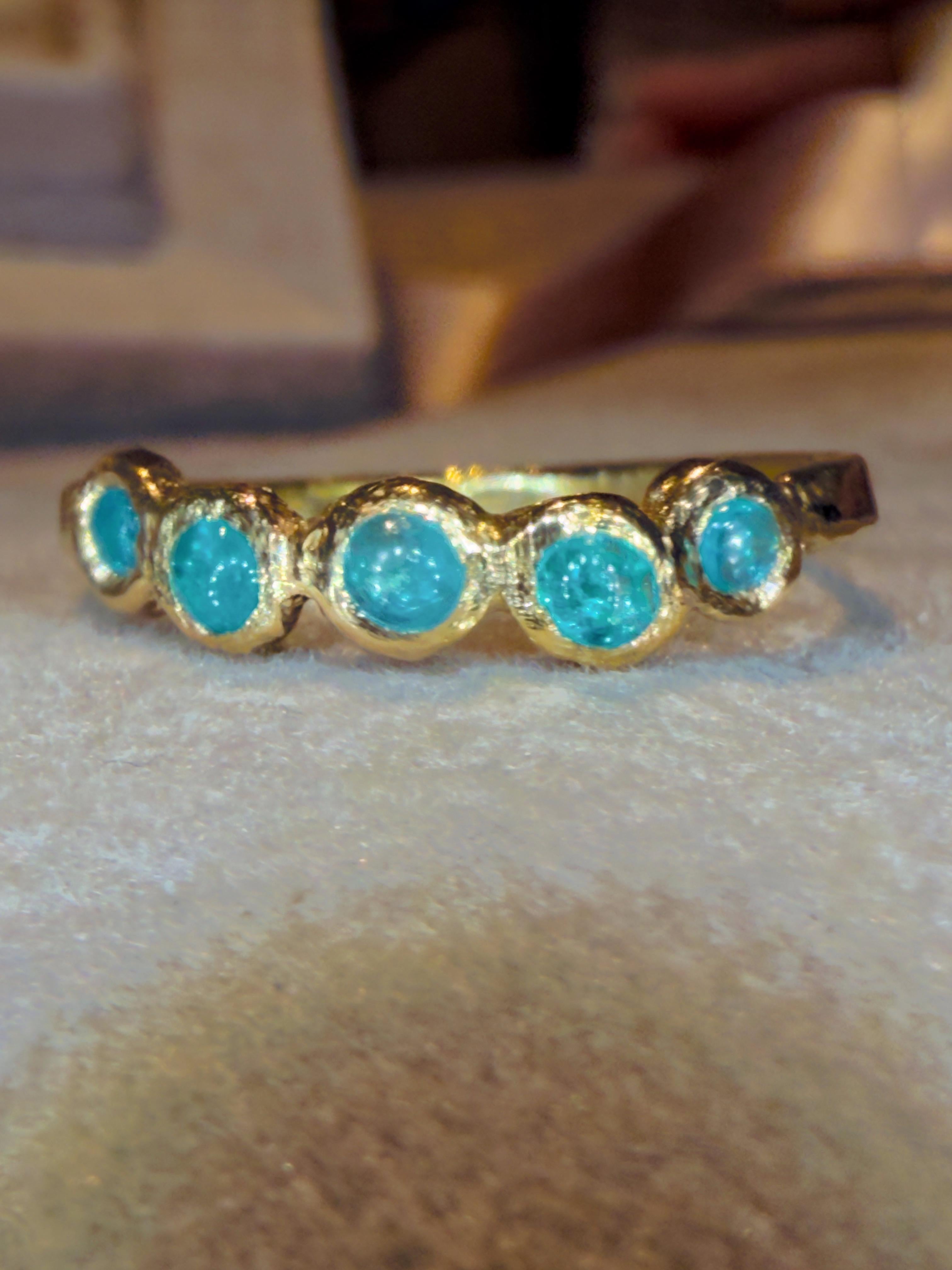 Un anello giocoso e allo stesso tempo elegante, realizzato a mano in ricco oro giallo 18 carati e caratterizzato da una fila di vivaci tormaline Paraíba. Ogni pietra è incastonata in un morbido castone organico che crea un ritmo fluente di punti blu