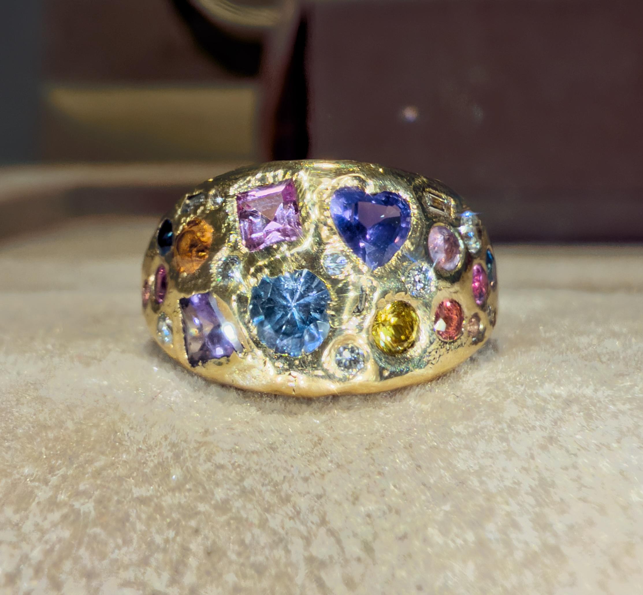 Una galassia di zaffiri, diamanti e arcobaleni di colori, tutti racchiusi in un anello a cupola in oro 18 ct. Ogni pietra è accuratamente incastonata a mano, creando una vibrante costellazione di forme e tonalità che brillano da ogni angolazione. Un
