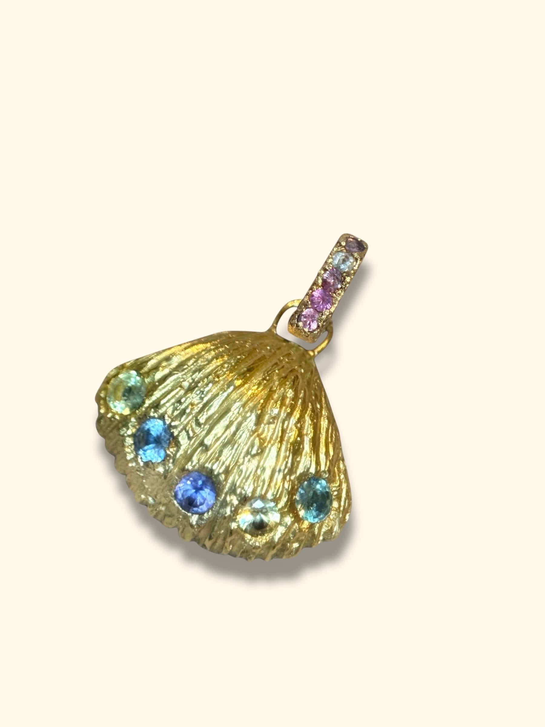 Questo squisito gioiello è caratterizzato da una conchiglia artigianale unica nel suo genere, meticolosamente realizzata in oro giallo 18 carati. L'intricato design della conchiglia è ornato da un'incredibile serie di zaffiri color pastello, che