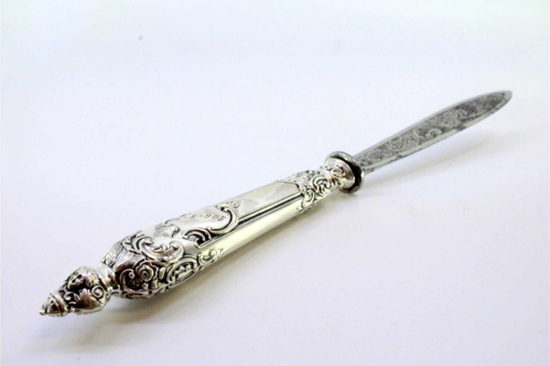 Description: Letter opener in the shape of a knife with an embossed silver handle and masks. 
Metal: Silver. 
Origin: European. 
Brand: Unknown. 
Weight: 39.42 grams. 
Dimensions: 22x1.7cm. 
Content: 900/1000. 
Assay Mark: Yes. 
Additional