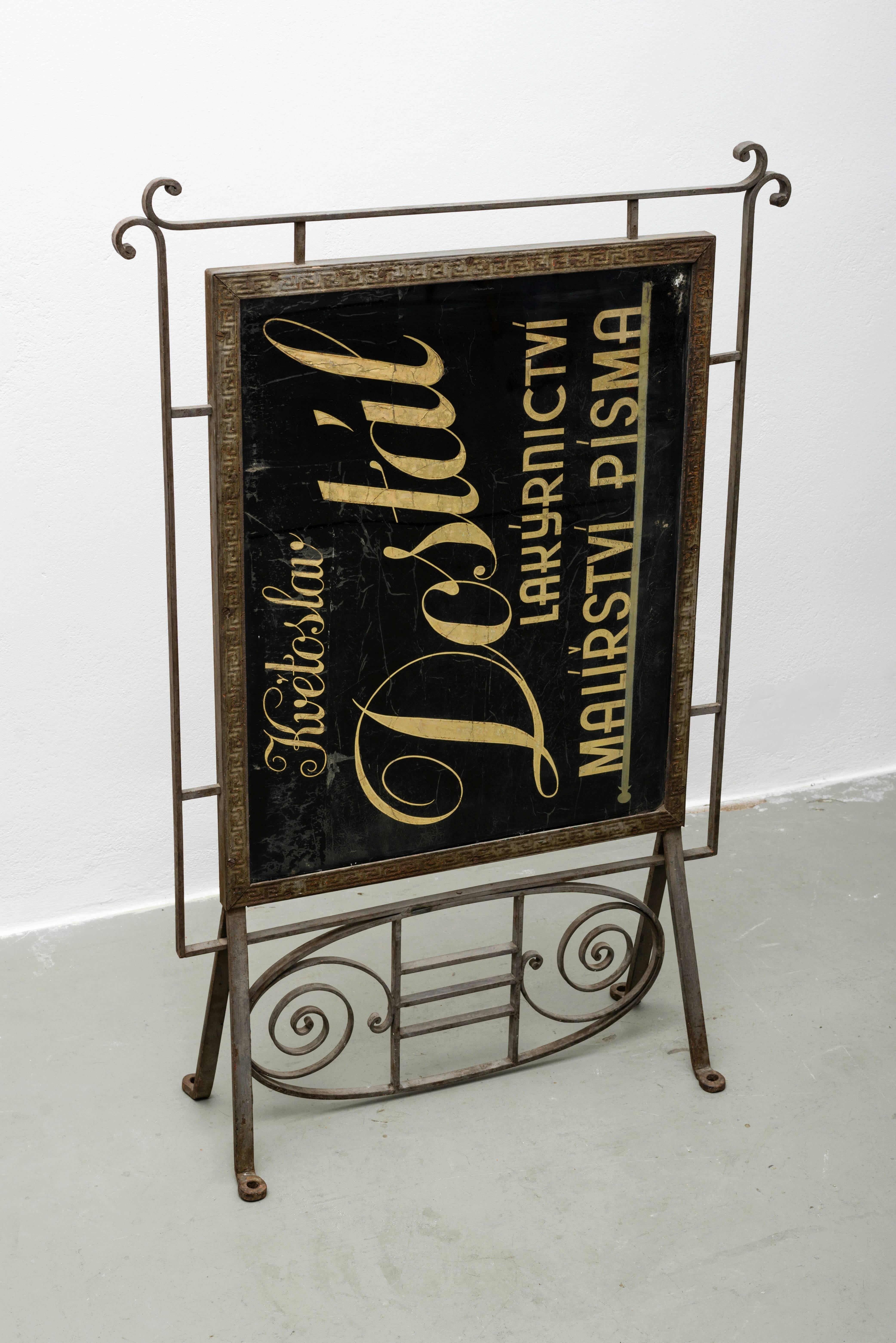 This vintage sign comes from the shop of Prague letter painter Kvetoslav Dostal. It was probably manufactured circa 1900, as the wrought iron frame construction shows Art Nouveau influences. The sign remains in a very good vintage condition with