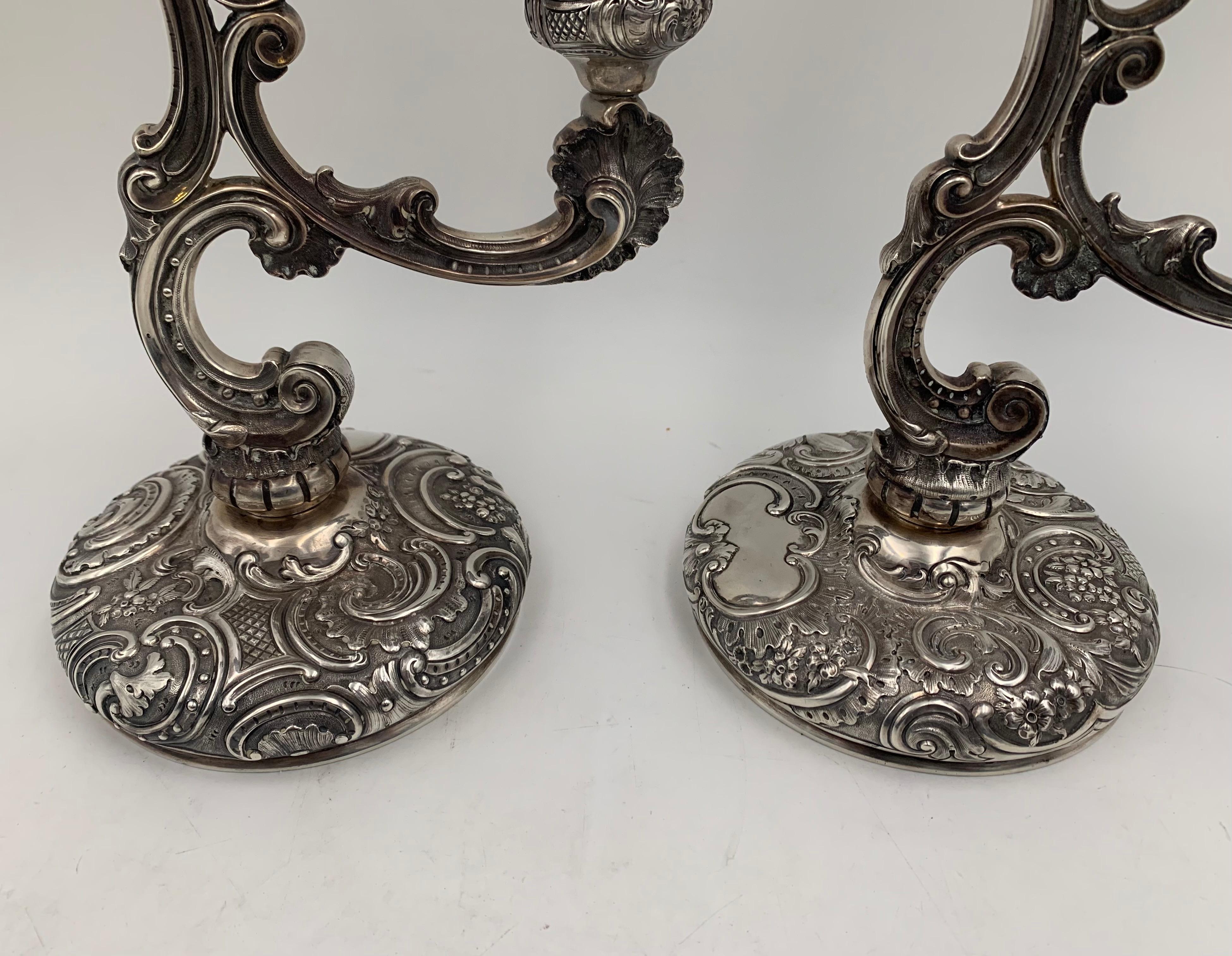Pair of finely chased, 3-light English sterling silver candelabra by William Leuchars from 1889 with removable bobeches in ornate Rococo style with floral motifs and stylized, curvilinear designs. Each measures 11 1/2'' in height by 9 1/2'' in width