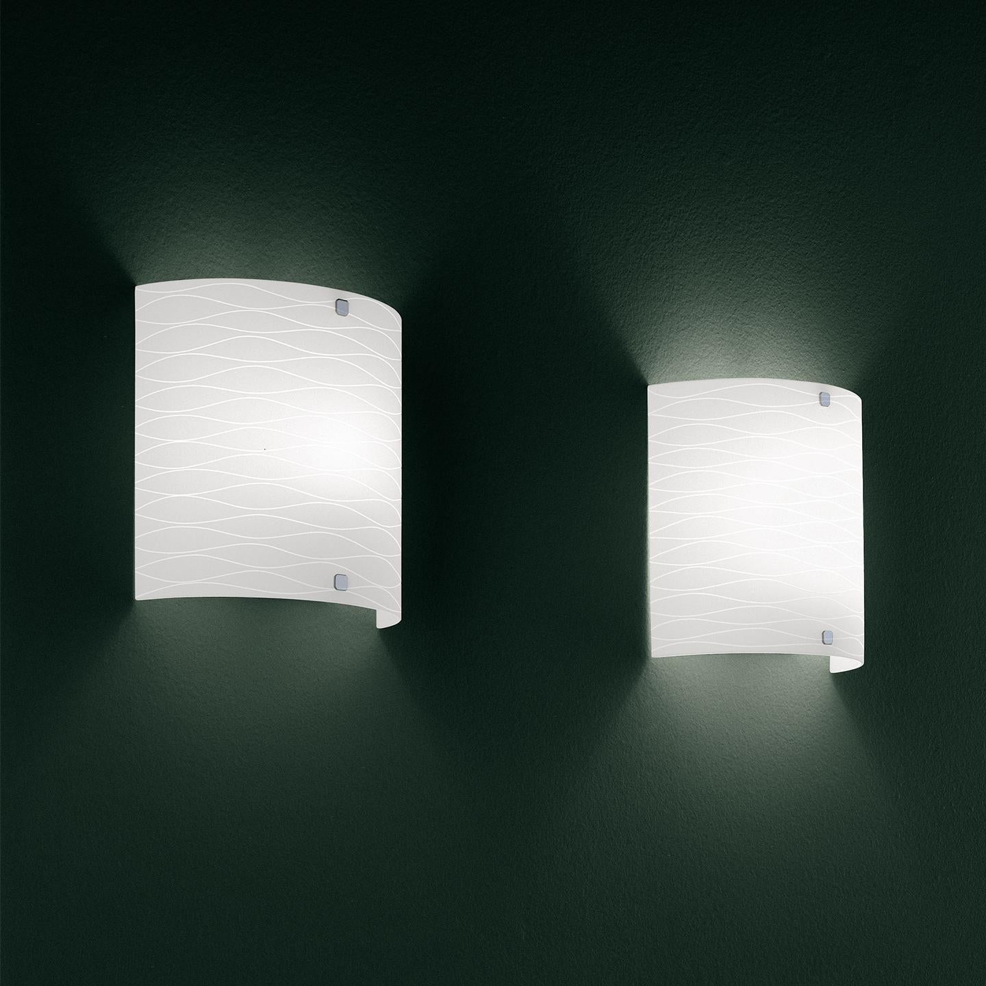 The class wall lamp was designed by Leucos design lab to be a fun, elegant lighting solution. The glass is hand-blown in Italy with a beautiful, wave-like horizontal etch detail. Compact overhang (ADA compliant). The class collection includes a
