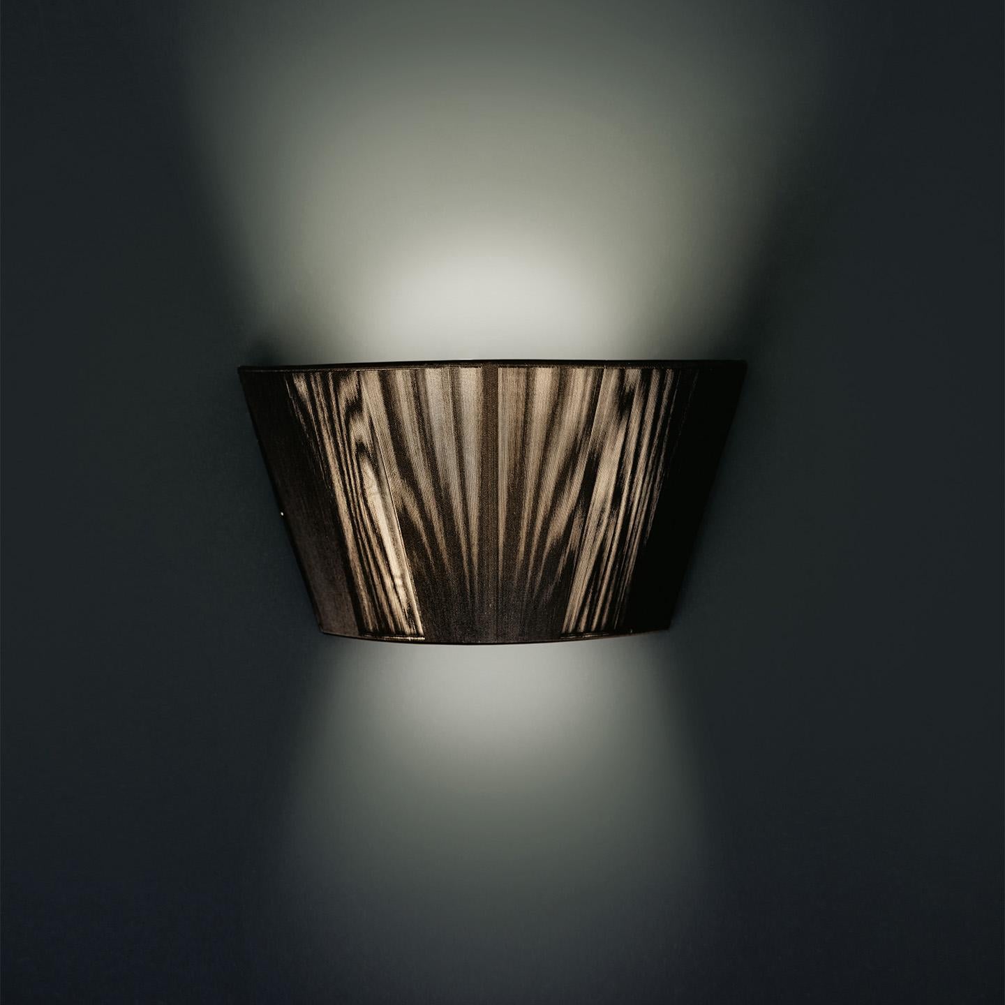 The Lilith wall lamp is an elegant lighting solution with a stunning light effect created by threading thin string in a consistent pattern across the shade. As you engage it from different viewpoints, the light pattern shimmers and changes. The