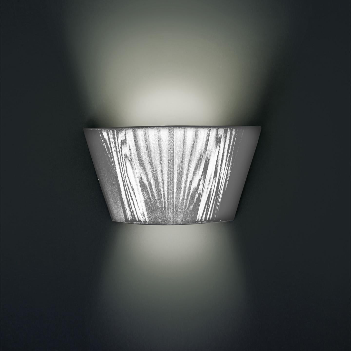 The Lilith wall lamp is an elegant lighting solution with a stunning light effect created by threading thin string in a consistent pattern across the shade. As you engage it from different viewpoints, the light pattern shimmers and changes. The