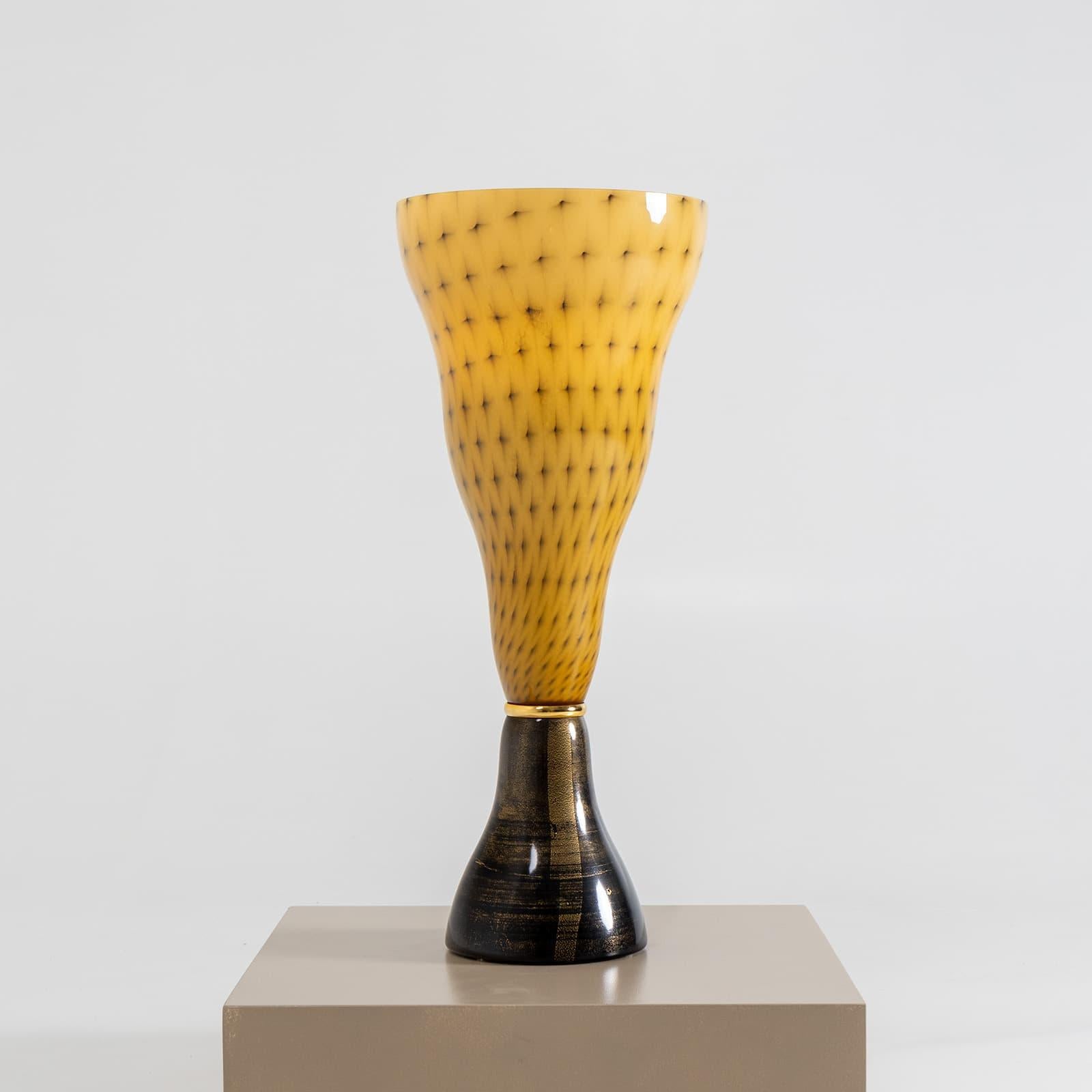 This striking funnel-shaped table lamp from the Vivia Collection features a distinctive amber color with dot decoration. It stands on a dark base with a gold-plated ring mount, adding a touch of elegance. The lamp is marked with the Leucos label on