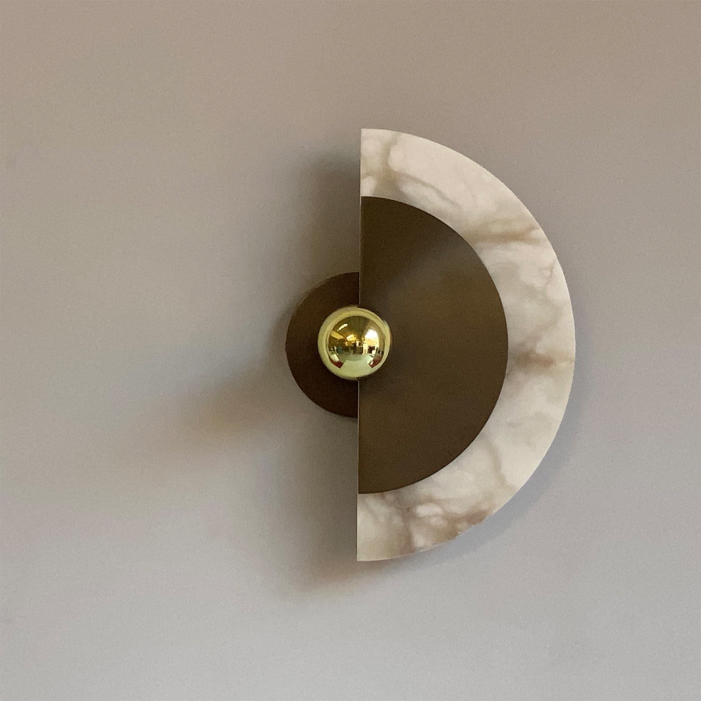 This charming wall sconce is truly ingenious in its unique design and craftsmanship. Featuring two half disks of elegant bronze and magnificent Italian alabaster. The disks can be rotated 30° on the central arm, forming a stunning interplay of