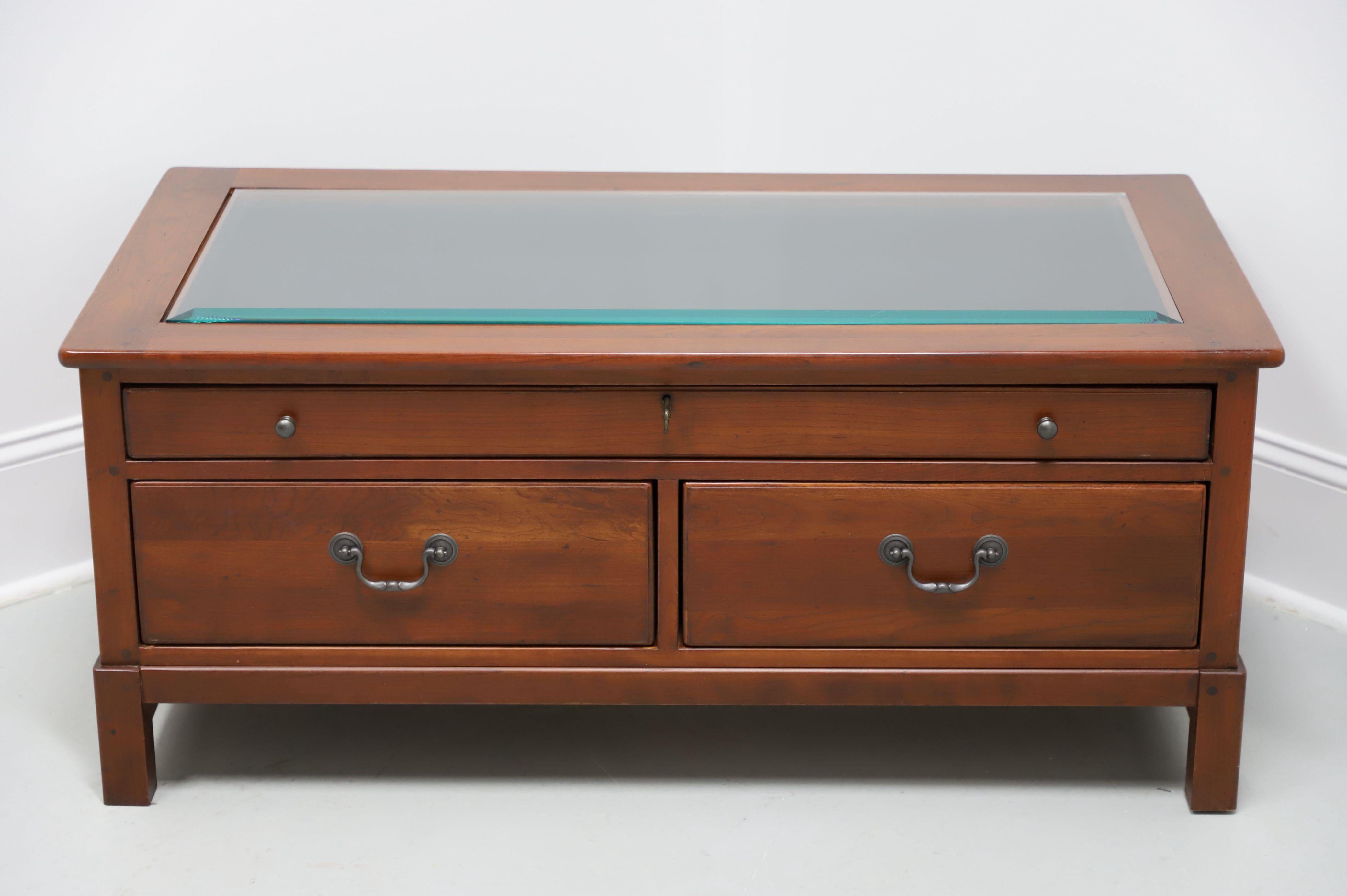 An Arts & Crafts style display cocktail table by Lexington Furniture, from their Bob Timberlake Collection. Solid cherry wood with brass hardware, rounded edge top with inset beveled glass, slide either way drawers, and elevated on straight legs.