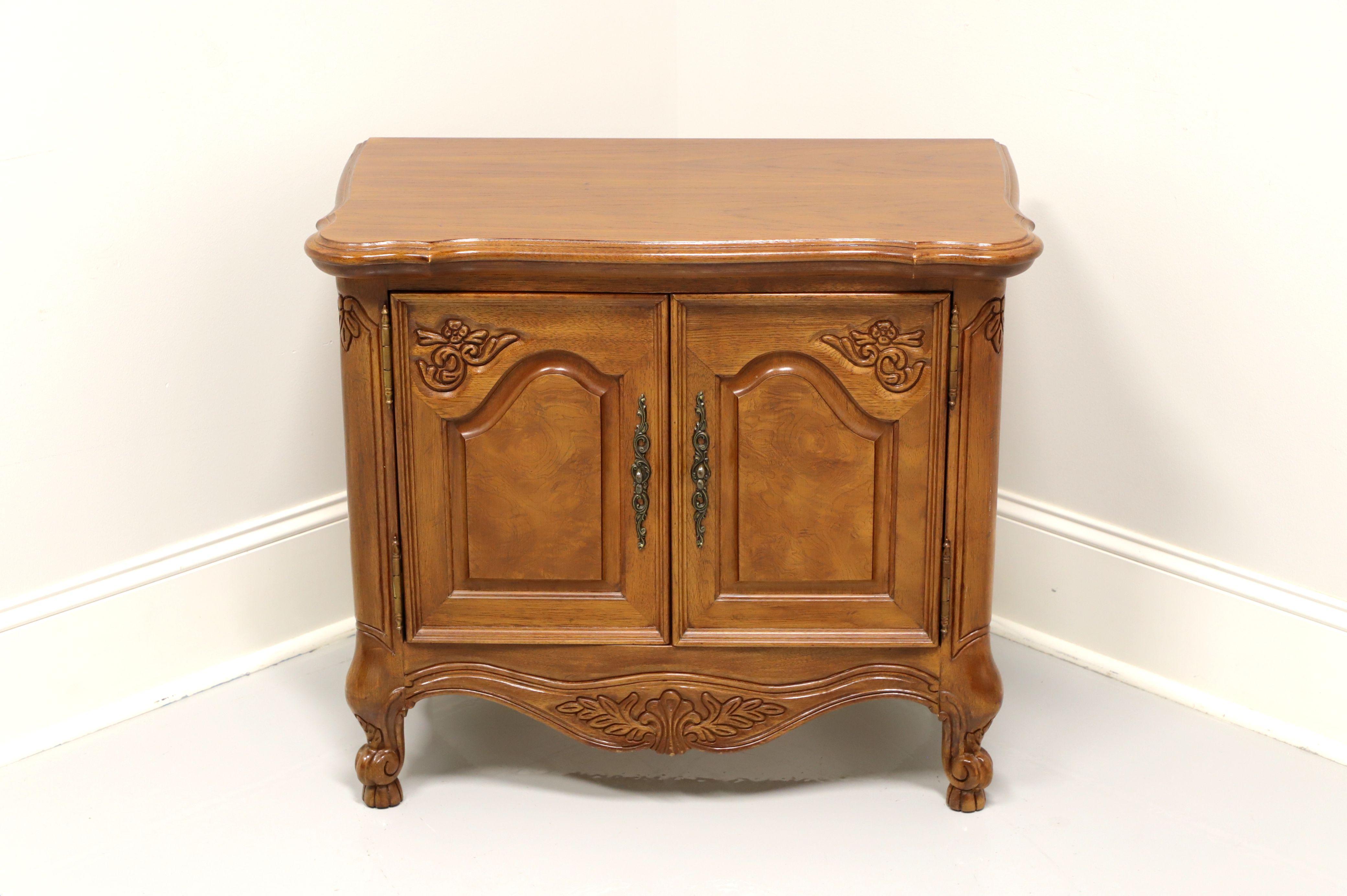 A French Country style nightstand by Lexington, from their Chateau Latour Collection. Walnut with brass hardware, curved front, carved apron and scroll feet. Features two door cabinet revealing one drawer of dovetail construction and storage area.