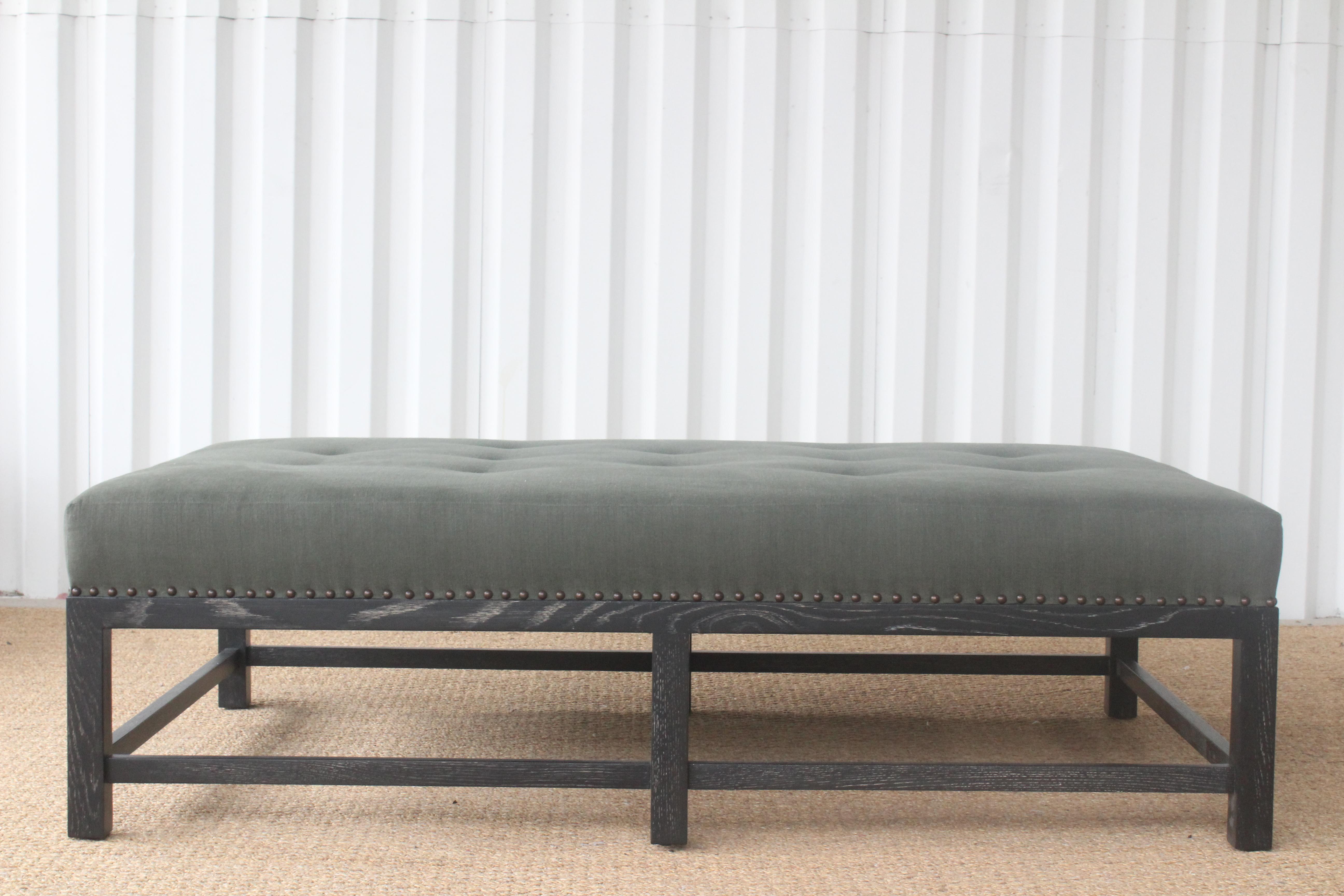 Custom made Lexington ottoman with an oak base and upholstered in a vintage dead stock vintage Belgian linen in olive green. The oak base is in a cerused satin black finish. Finished with antique brass nailhead trim. Handmade in Los Angeles.