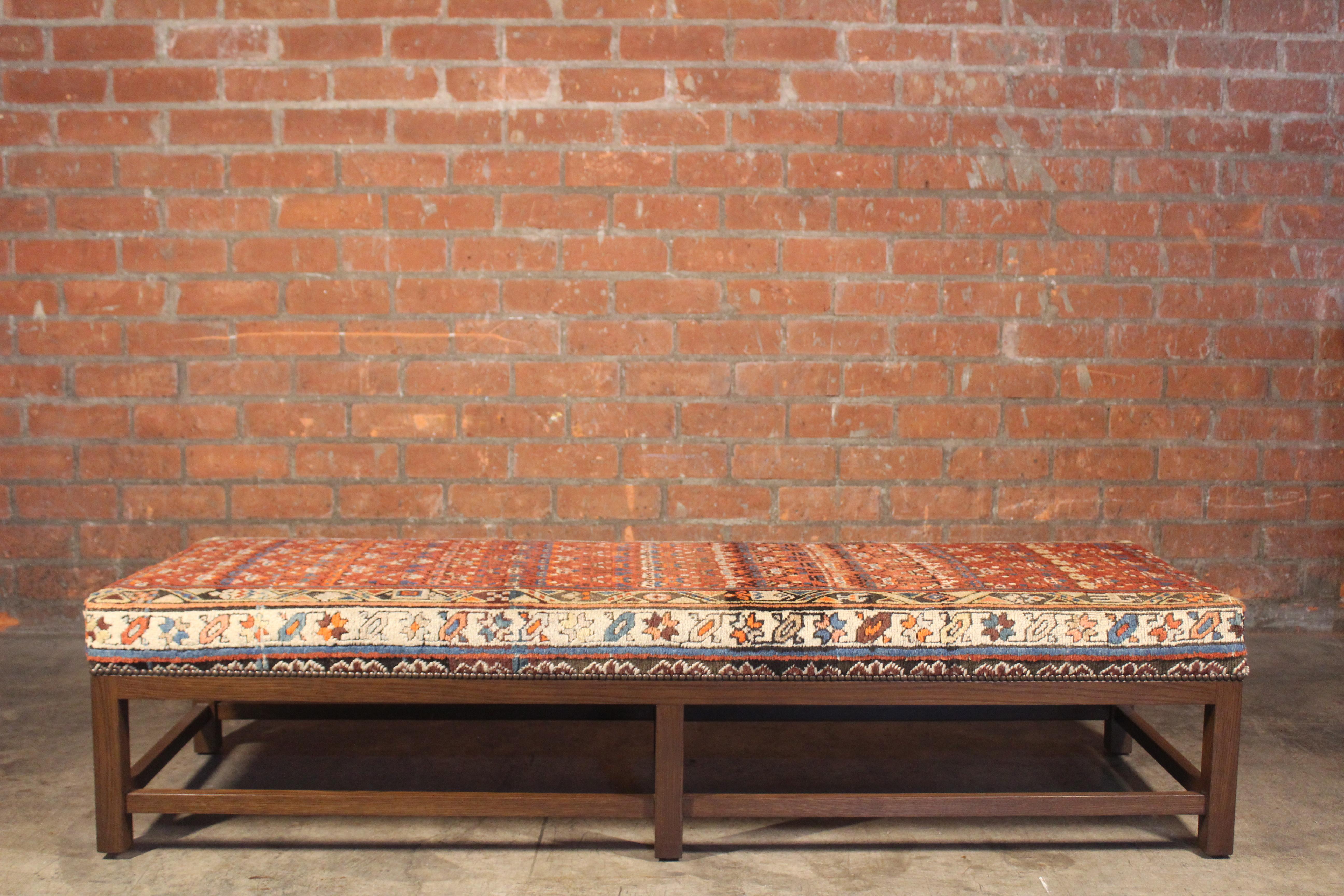 A custom made Lexington ottoman or bench, upholstered in a vintage Turkish rug. The base is solid oak in a dark finish with brass nail head details. The rug was cleaned prior to upholstery. Perfect as an ottoman or a bench at the foot of a bed.