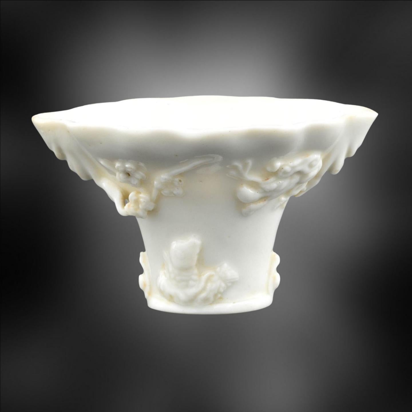 Blanc de Chine cup of a shape copying earlier cups which were carved from 16th century rhinoceros horns. 

Lucious Dehua porcelain, moulded and heavily sprigged with plum blossom, deer, phoenix, fish and dragons.

An attractive piece of moderate