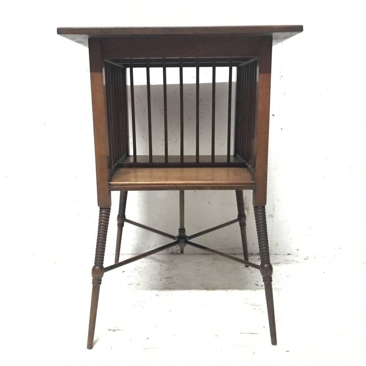Liberty & Co, a fine Anglo-Japanese Walnut side table in the style of E W Godwin with a spindle gallery below to two sides and a spindle divided lower shelf. The whole on sharply angled and ring turned legs uniting four stretchers with a central