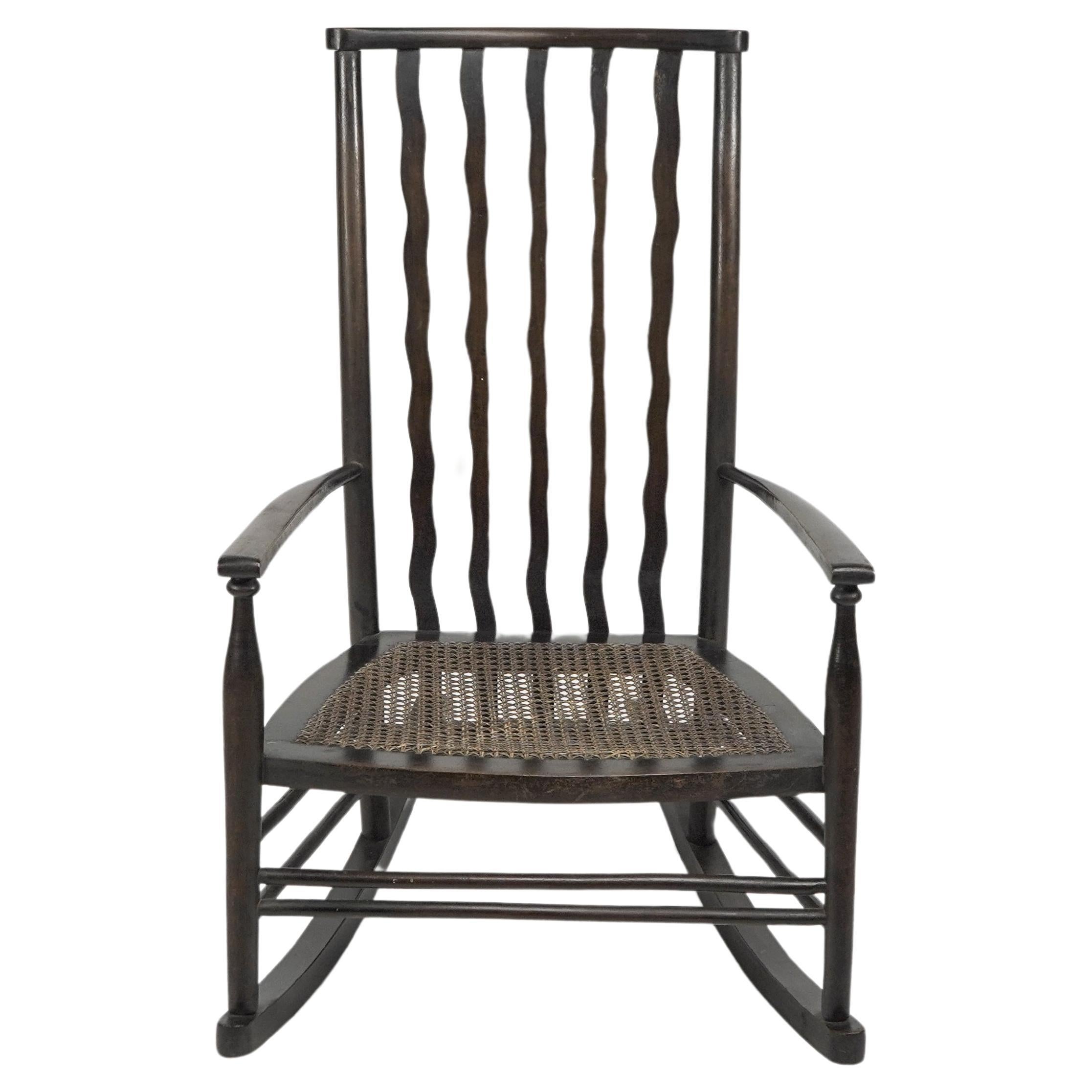 Liberty and Co. A sweet litte beech stained and original cane seated rocking chair with a wonderful wavy back flowing down while attatching to the rear of the seat then inserted into the lower back stretchers to strengthen it further. A fine