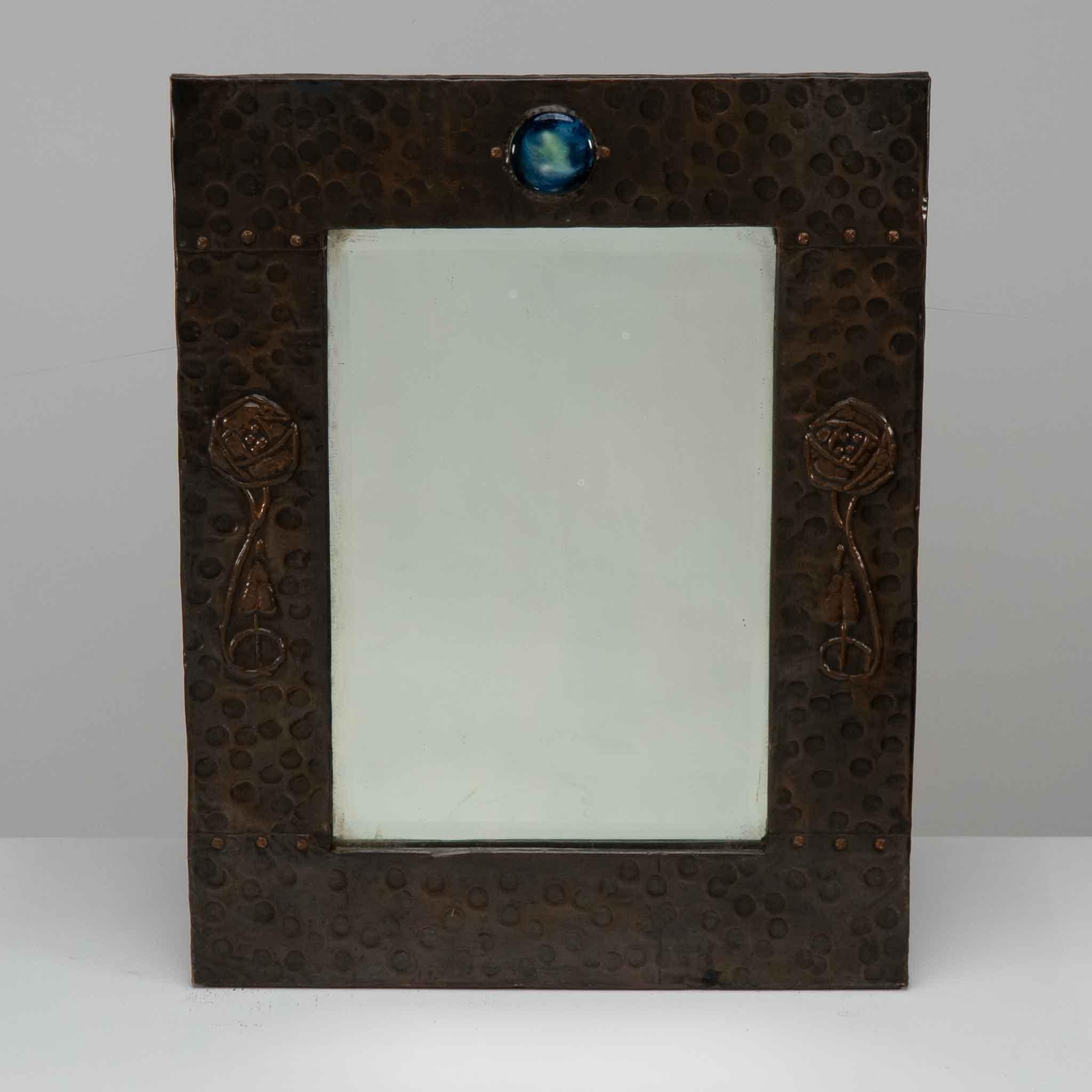 Liberty and Co. An Arts and Crafts copper mirror with a cloudy blue Ruskin Jewel to the top and Glasgow rose decoration to each side.