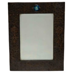 Antique Liberty and Co. An Arts and Crafts copper mirror with a cloudy blue Ruskin Jewel