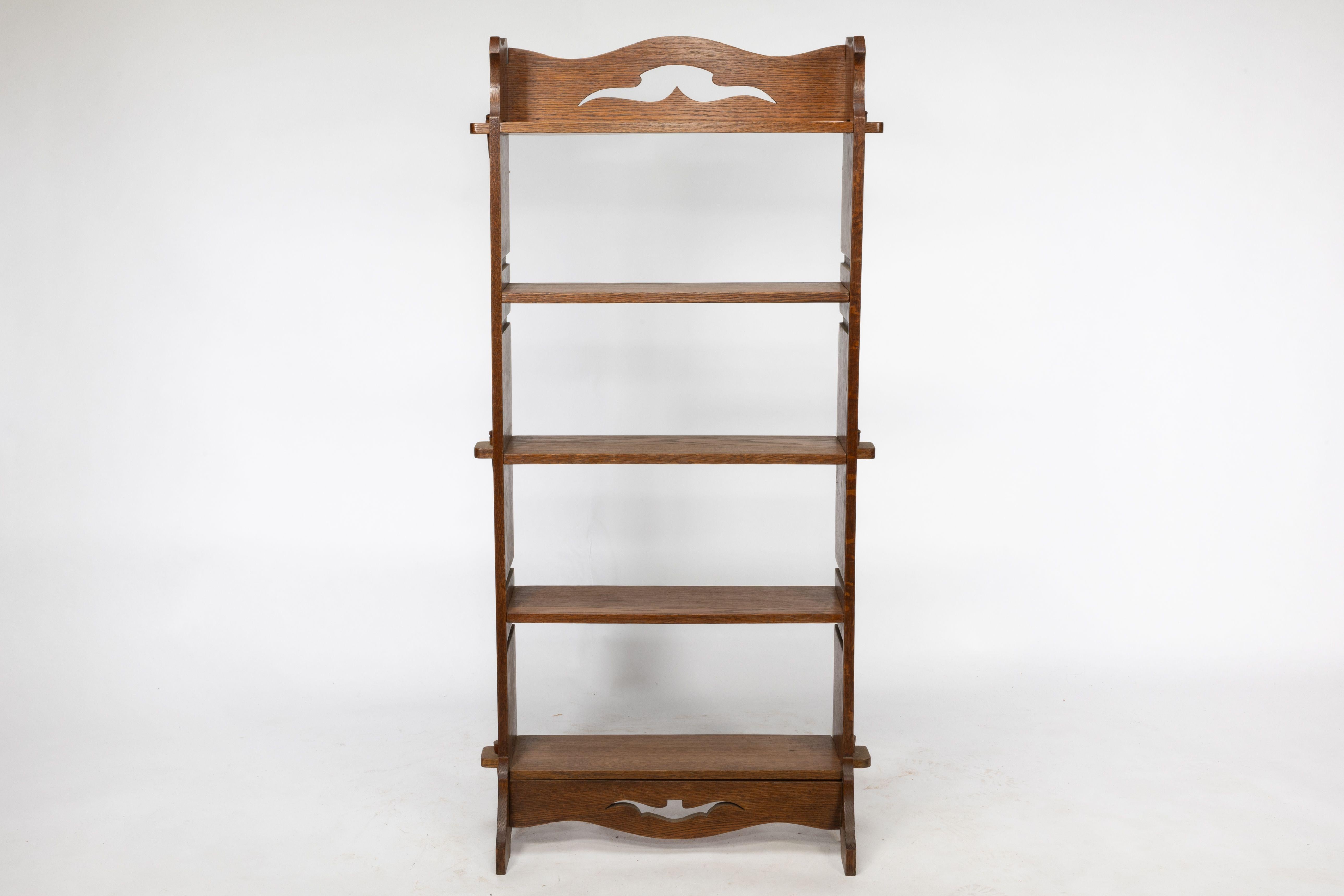 A Liberty and Co Arts and Crafts golden oak bookcase with unusual shelves that slide in from the back giving three different heights, with stylised floral cut-outs to the top and bottom and through pegged construction.