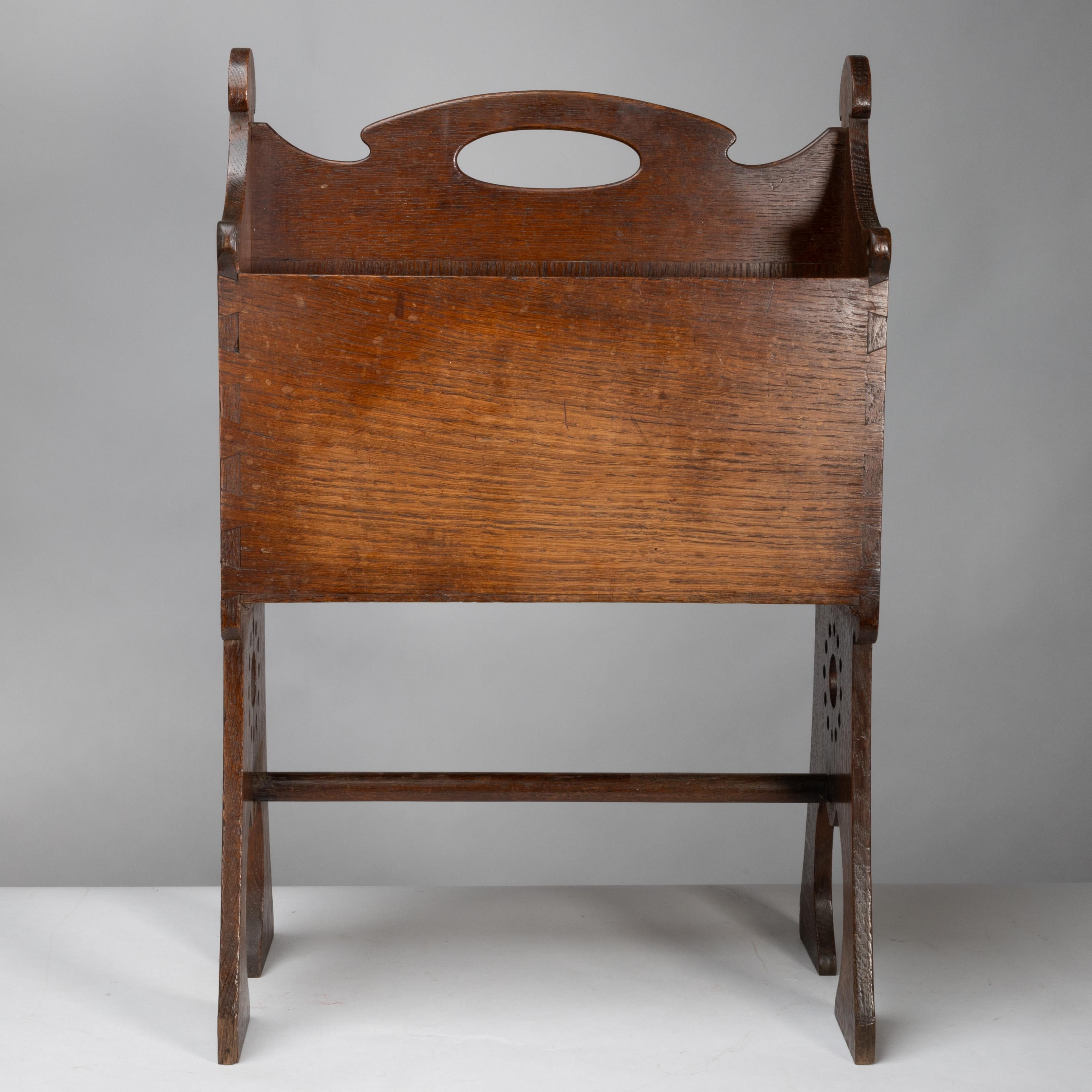 Liberty and Co. An Arts and Crafts oak magazine rack with a raised handle and twin compartments inside with pierced circular decoration to the sides on shaped legs united by a turned stretcher.